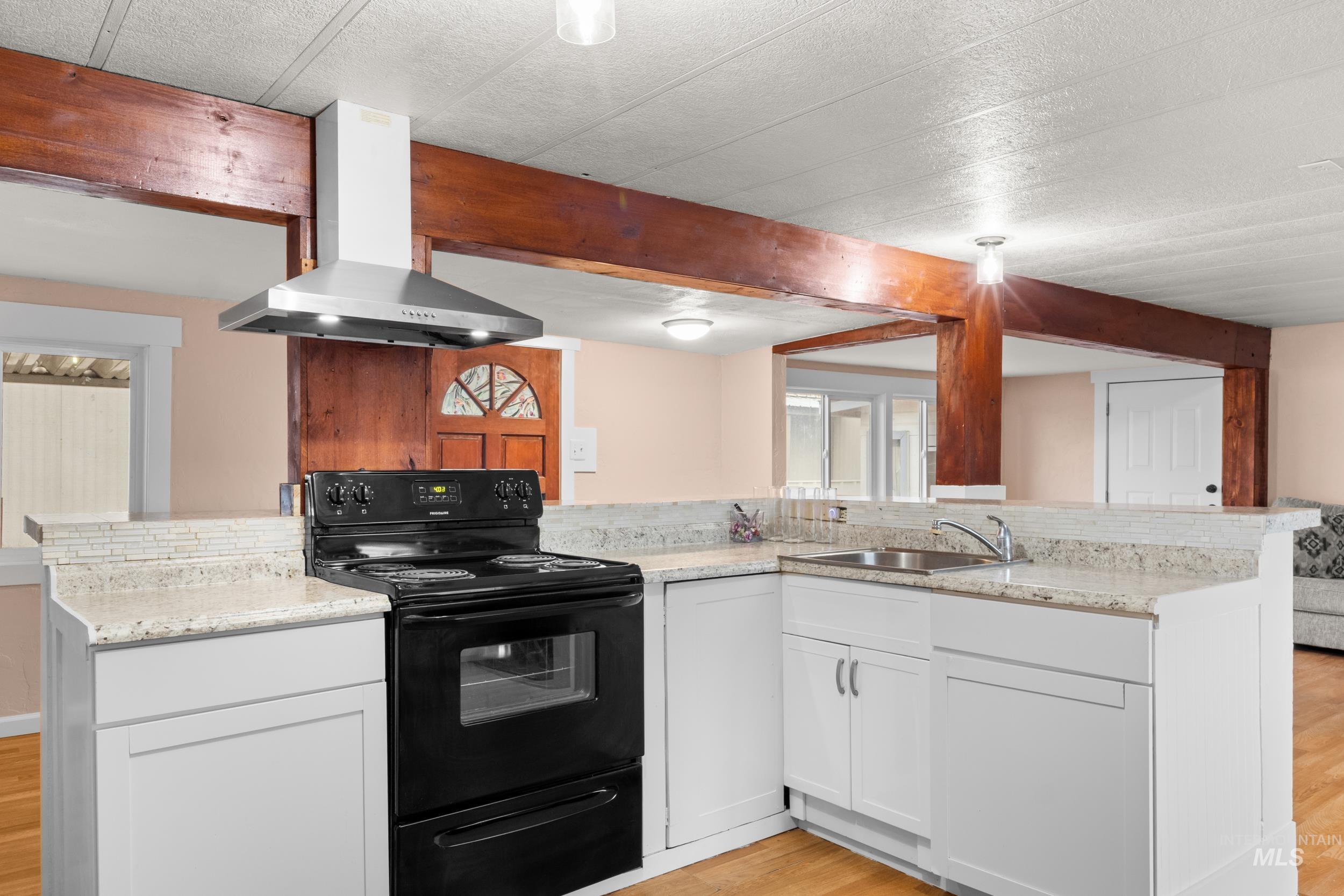 Kitchen with black / electric stove, white cabinetry, wall chimney range hood, light wood-style flooring, and a peninsula
