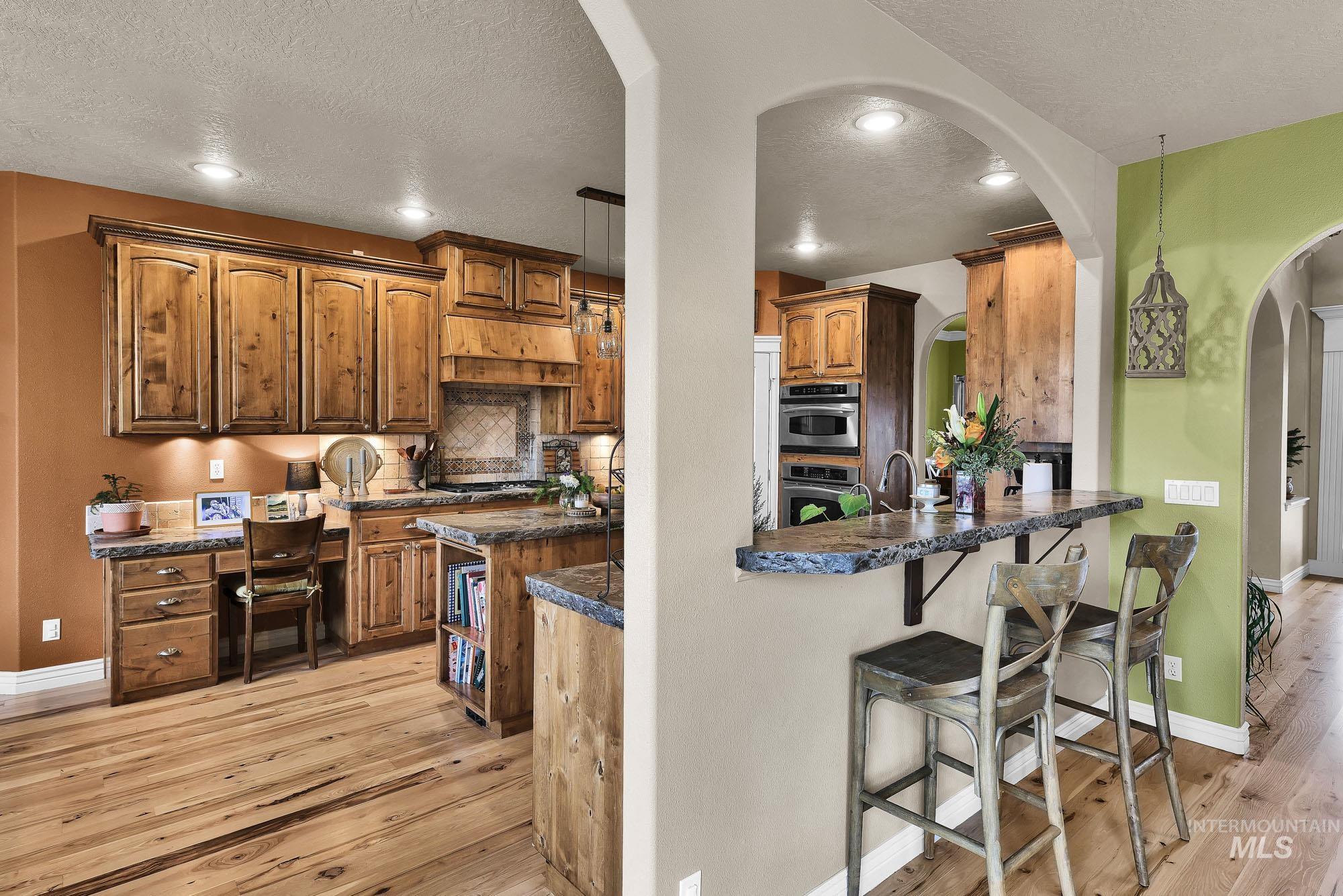 Kitchen featuring arched walkways, light wood-style floors, a breakfast bar area, pendant lighting, and tile backsplash