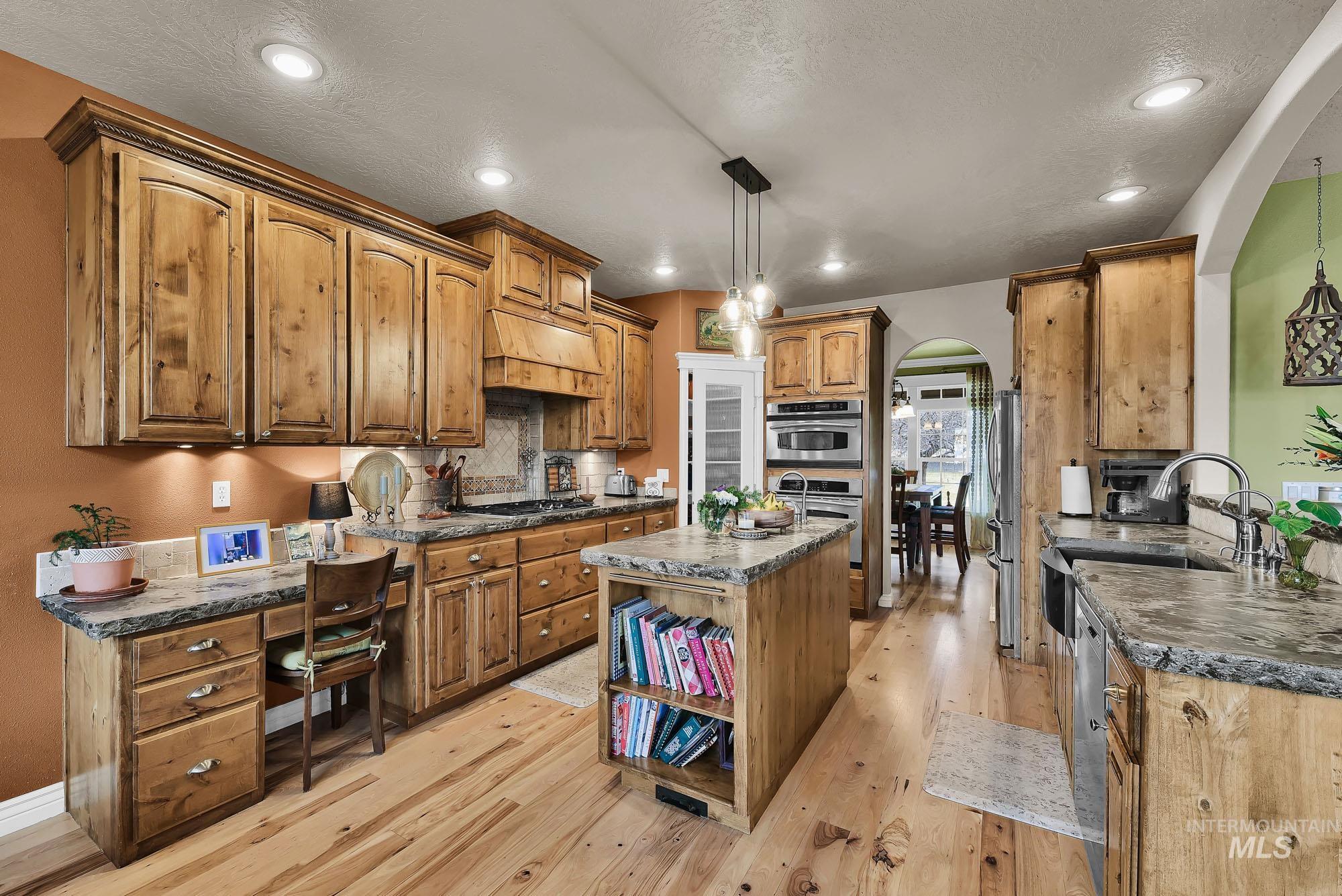 Kitchen with arched walkways, a kitchen island with concrete counter tops and veggie sink, pendant light fixtures, rustic Alder cabinetry and light refinished maple floors