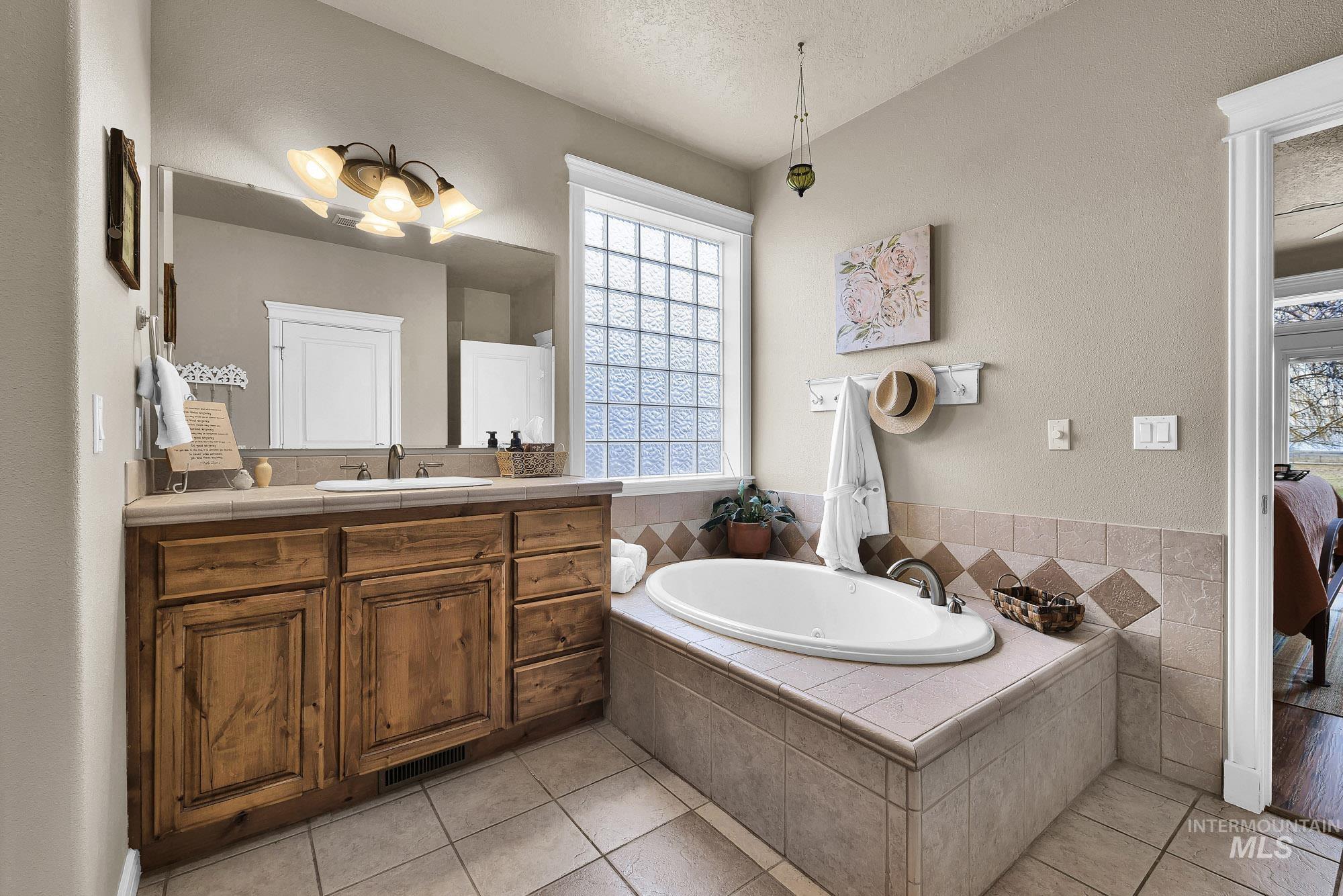 Primary Bathroom featuring dual vanities, a oversized jacuzzi bath, light tile patterned flooring, and huge walk in closet