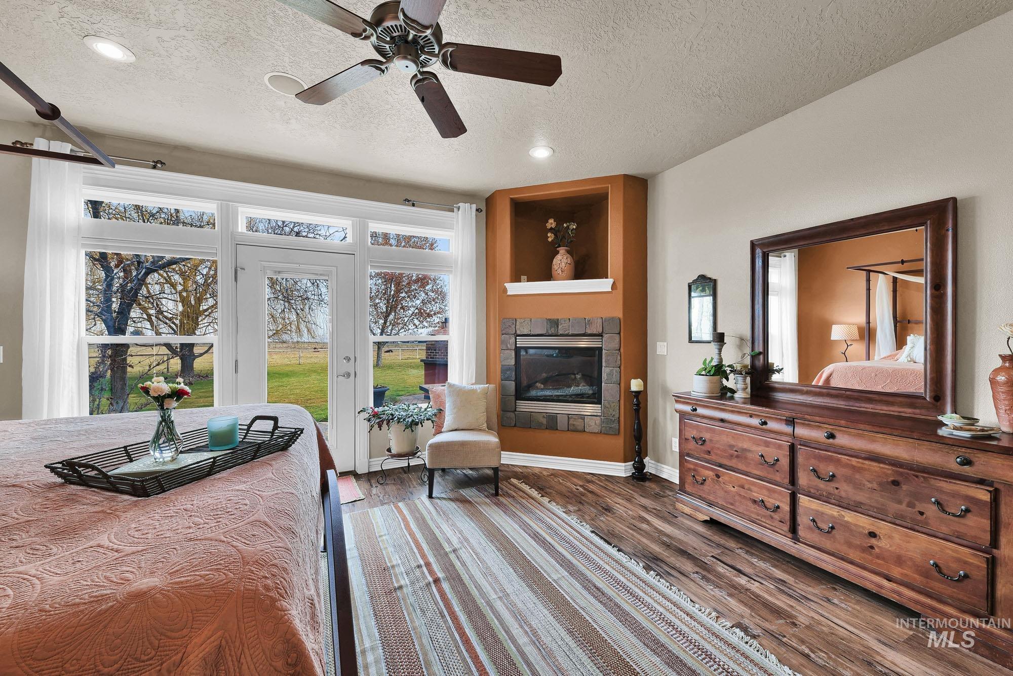 Primary Bedroom Suite featuring a ceiling fan, access to the back patio and hot tub, a gas tiled fireplace, engineered wood style flooring, and recessed lighting