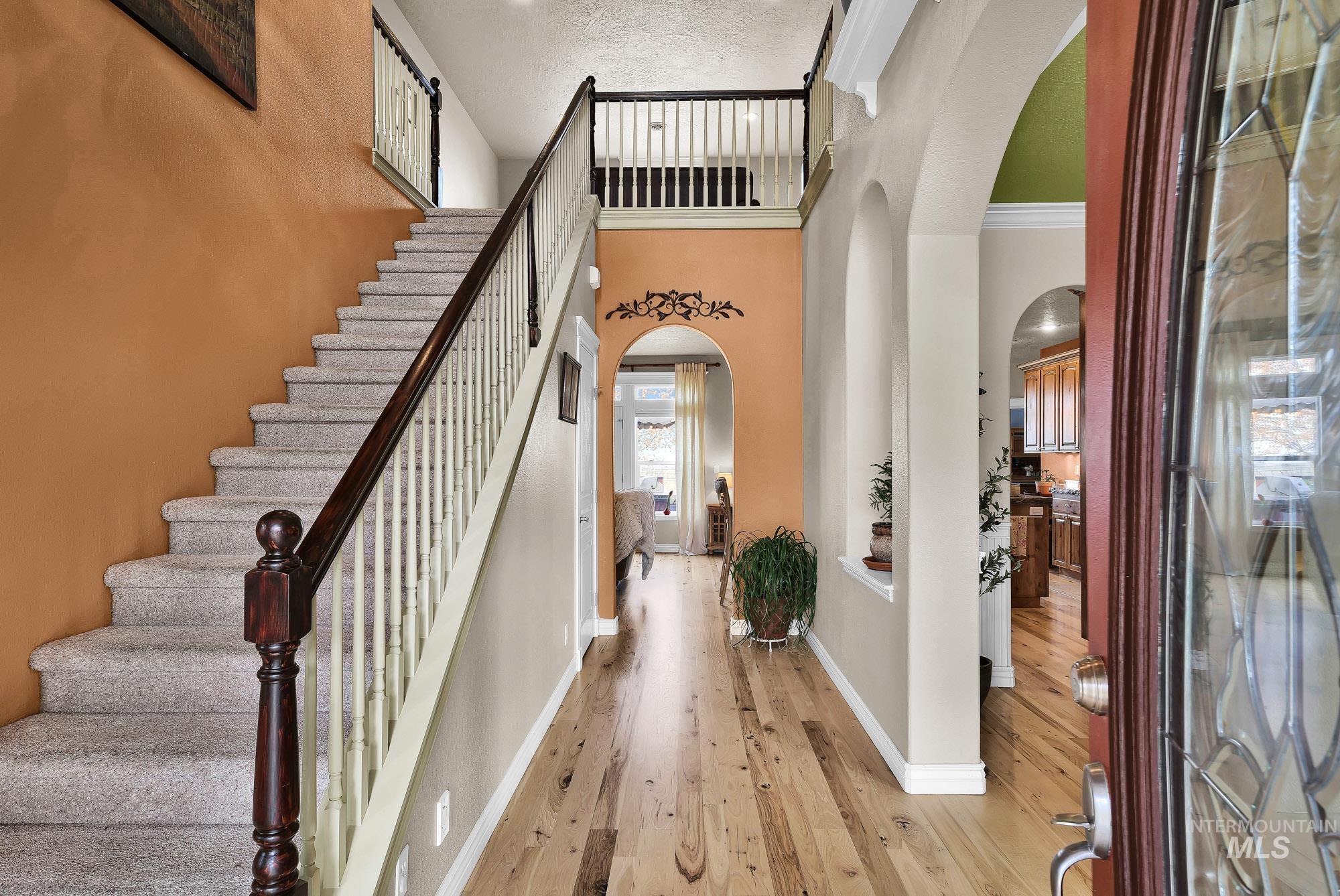 Foyer featuring arched walkways, light wood finished floors, stairs, and a high vaulted ceiling