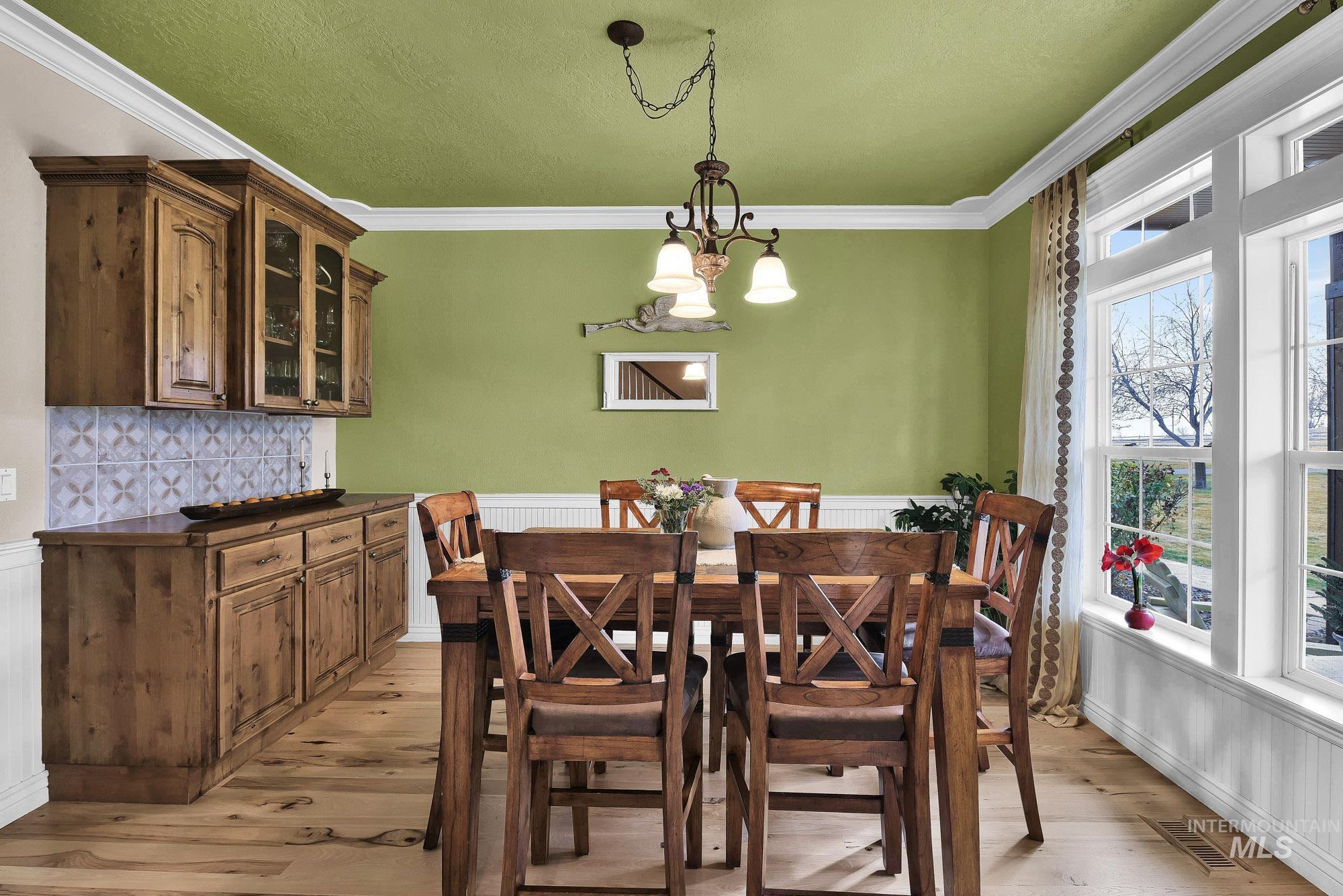 Dining area featuring a built in china hutch and buffet, light wood-style flooring, a wainscoted wall, a chandelier, and a textured ceiling
