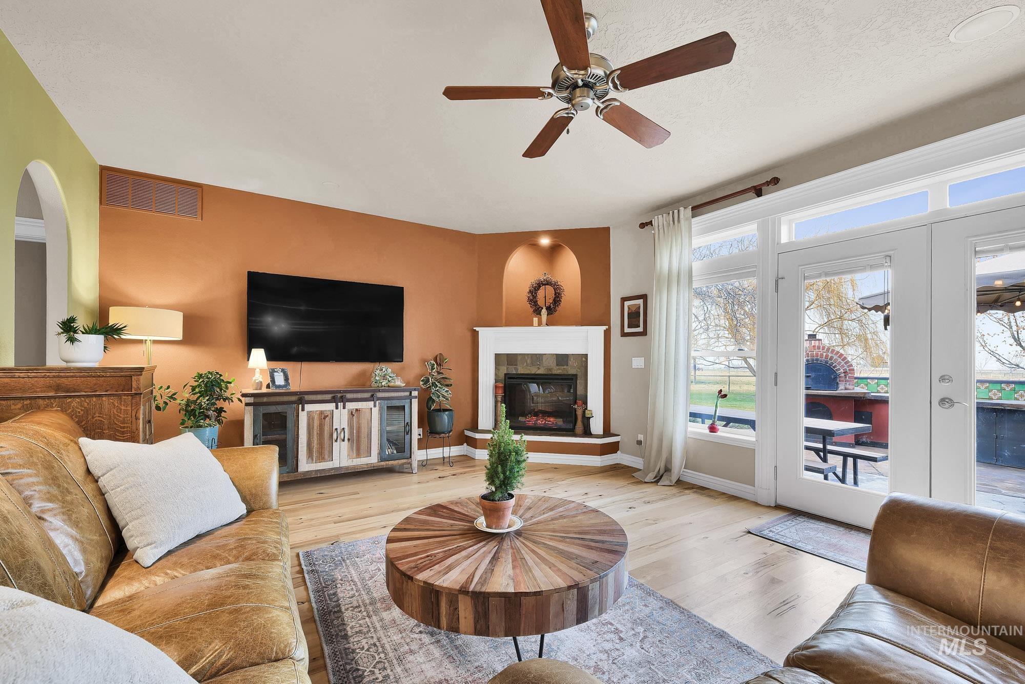 Living room featuring wood finished floors, a tile fireplace, expansive windows with transoms and a ceiling fan