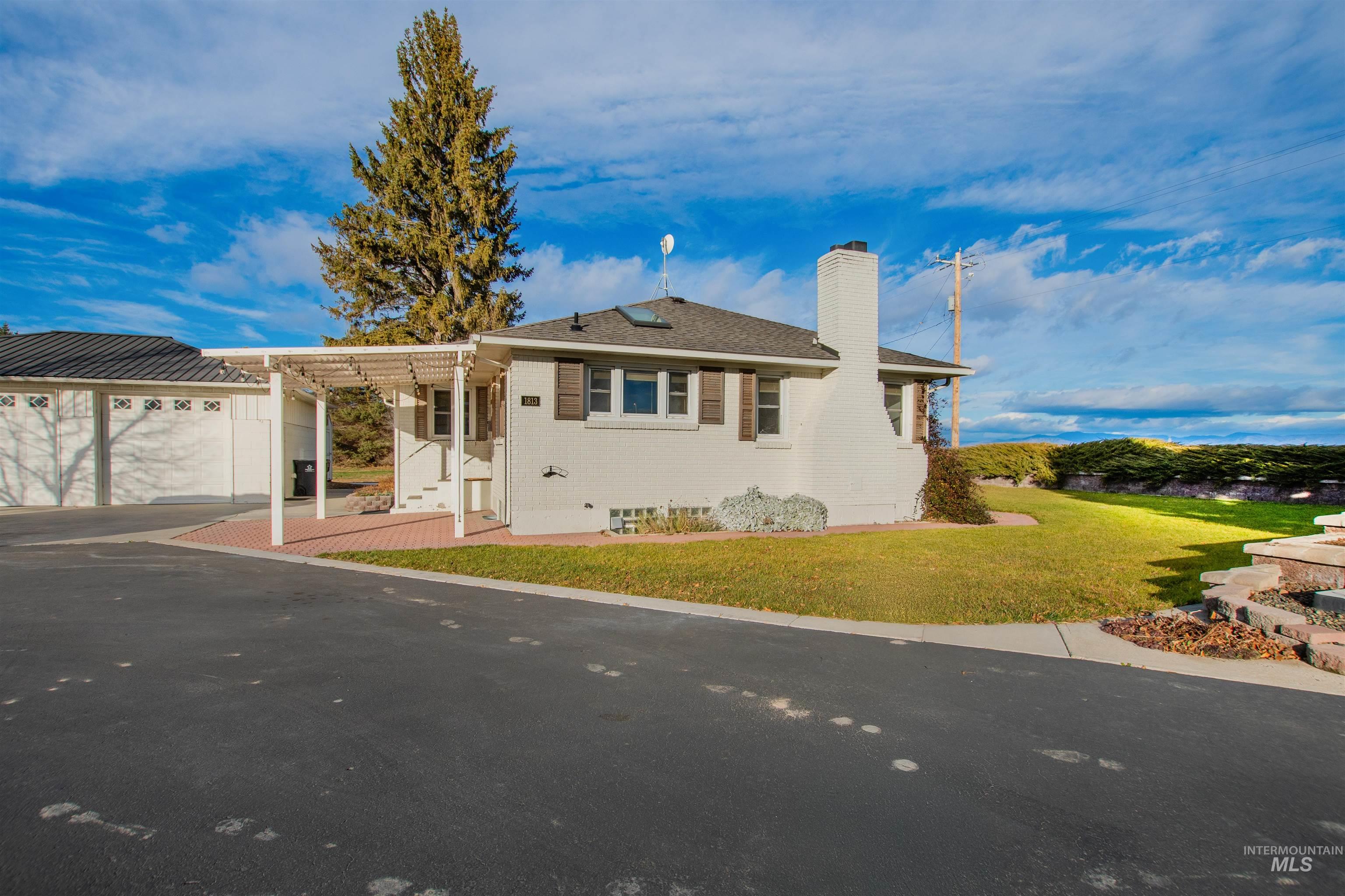 Ranch-style house featuring a chimney, a front yard, brick siding, a pergola, and driveway