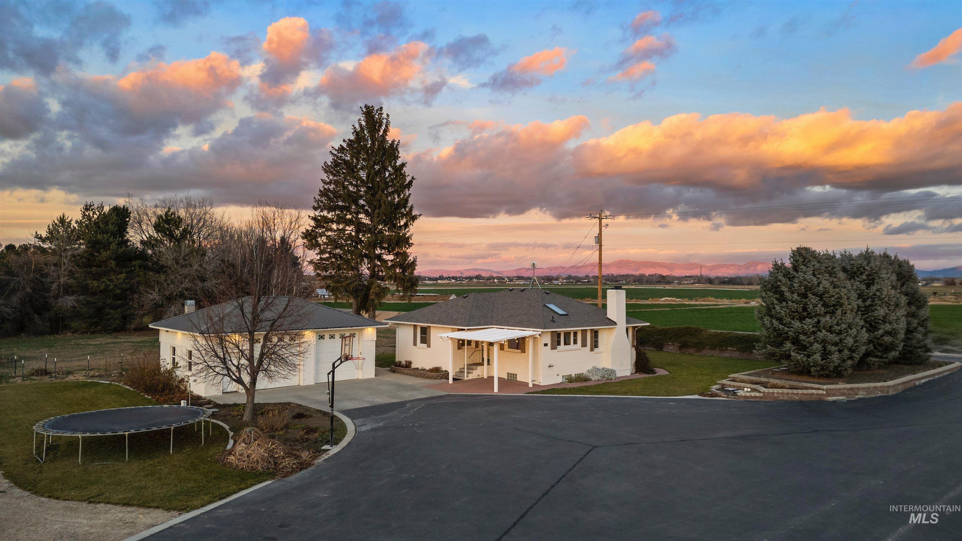 View of front facade featuring a trampoline, a chimney, a garage, a yard, and driveway