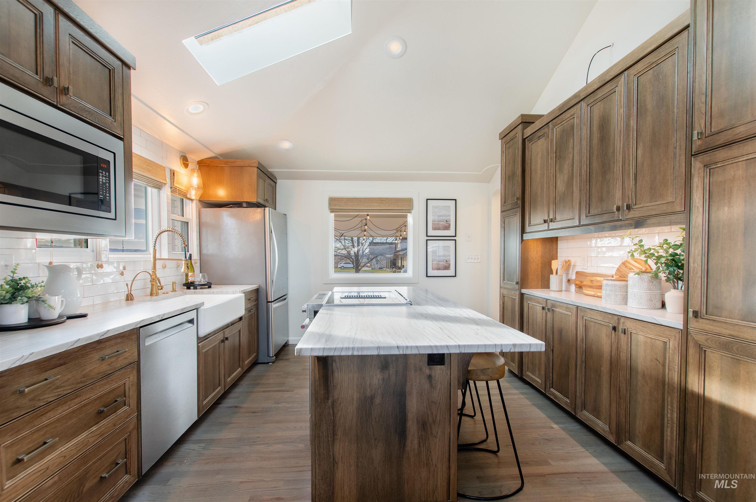 Kitchen featuring tasteful backsplash, a kitchen island, lofted ceiling, a skylight, and stainless steel appliances
