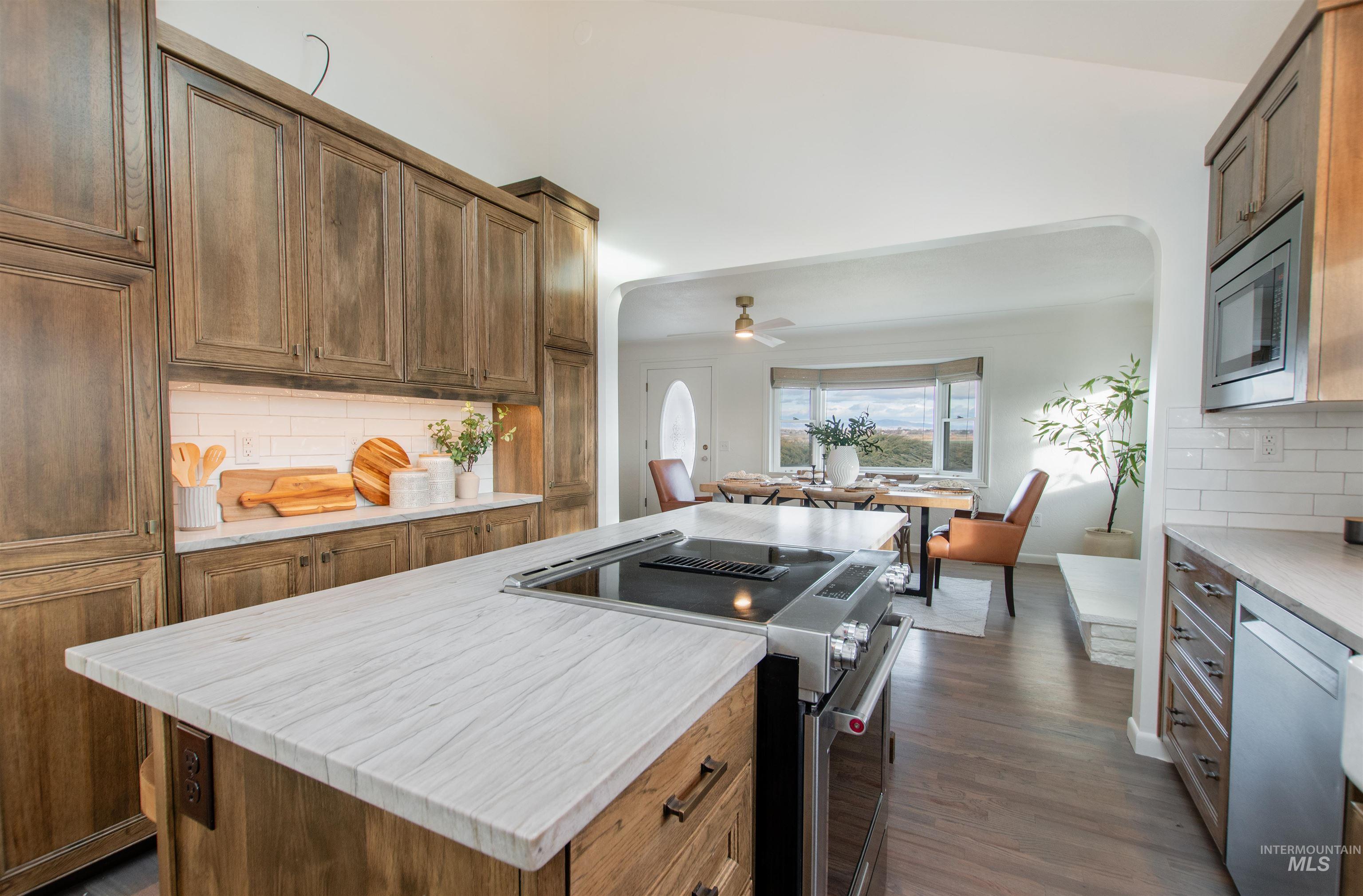Kitchen featuring backsplash, stainless steel appliances, arched walkways, open floor plan, and dark wood-style flooring
