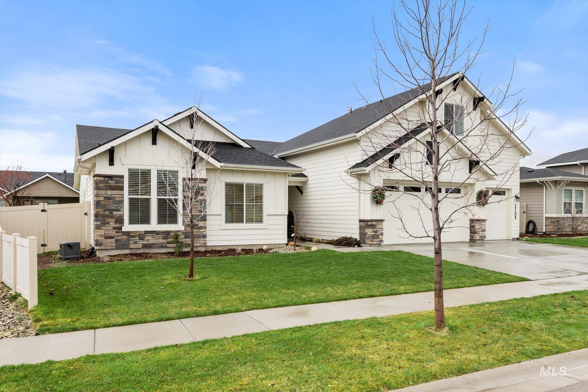 View of front facade with board and batten siding, stone siding, concrete driveway, and a shingled roof