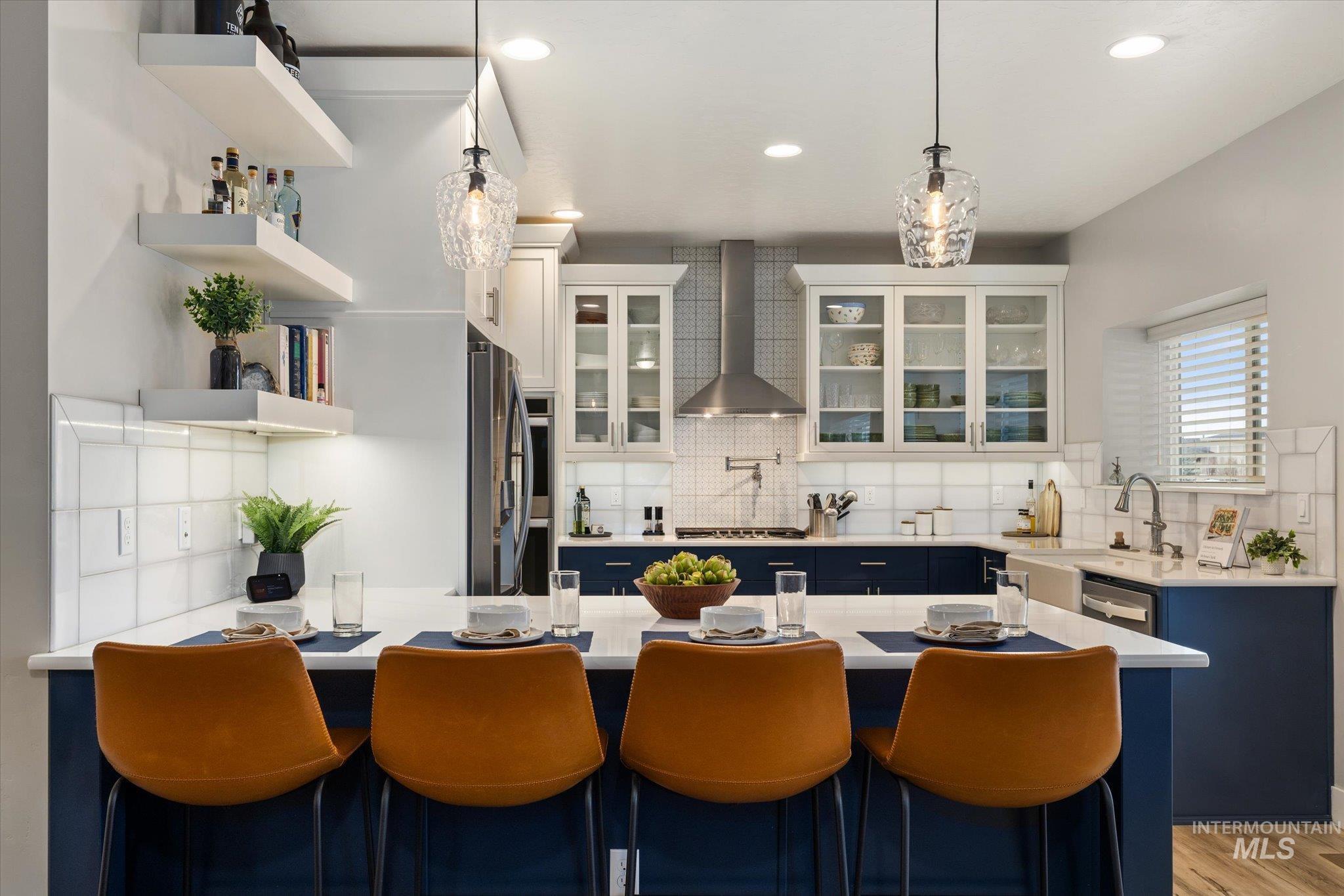 Kitchen with blue cabinets, a breakfast bar, hanging light fixtures, wall chimney exhaust hood, and decorative backsplash