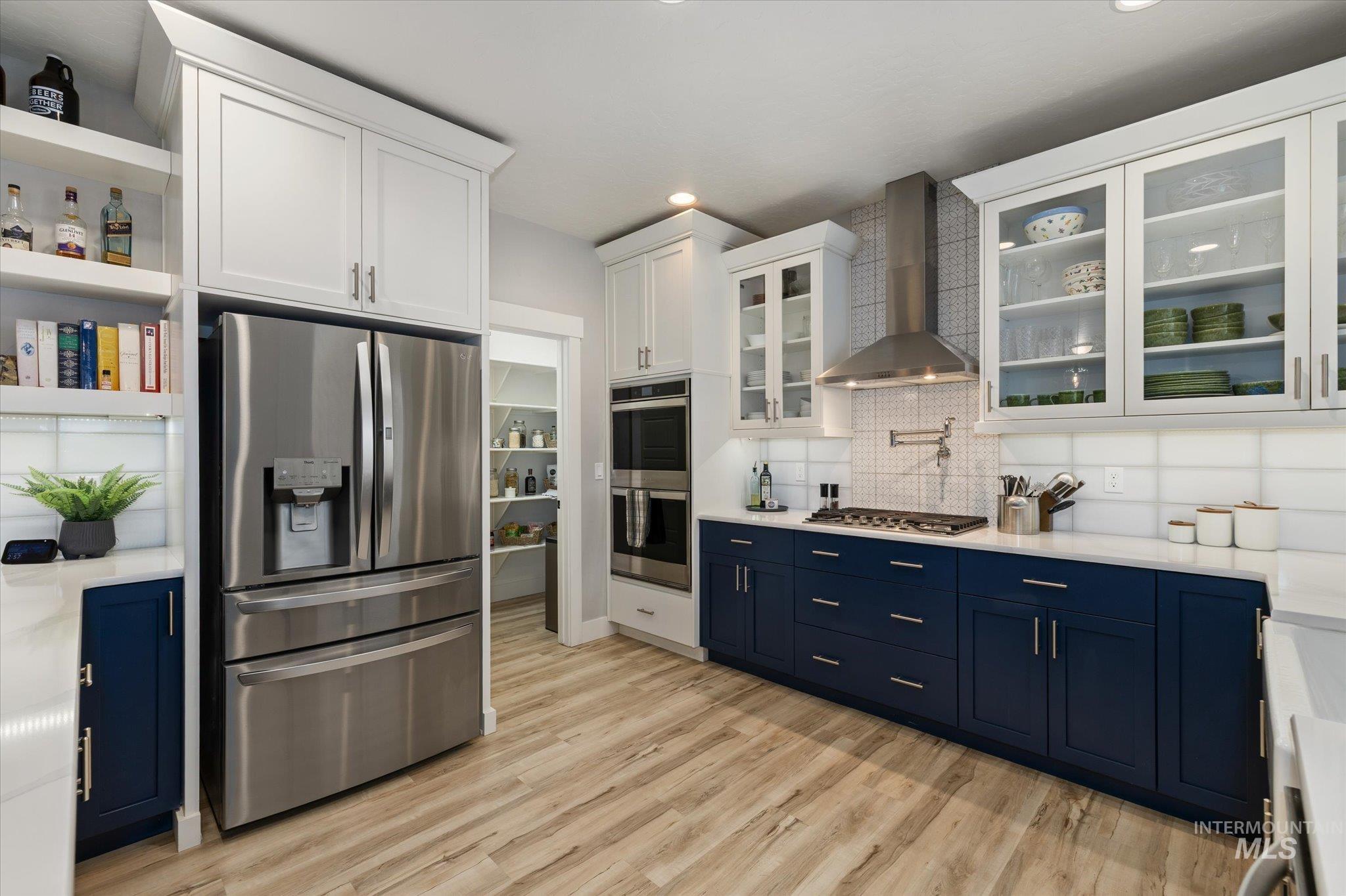 Kitchen featuring blue cabinets, open shelves, appliances with stainless steel finishes, wall chimney exhaust hood, and recessed lighting