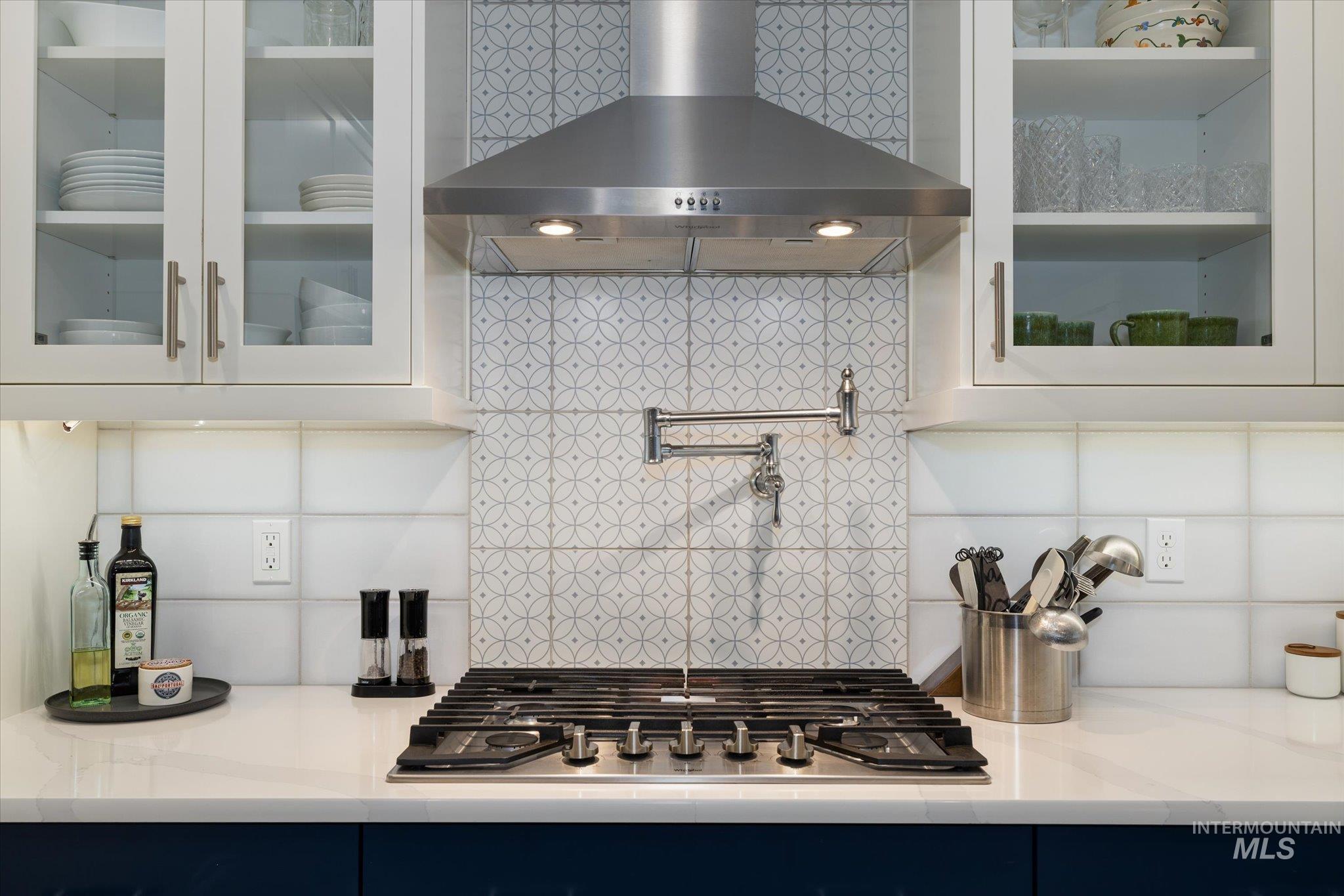 Kitchen with exhaust hood, glass insert cabinets, blue cabinets, and backsplash
