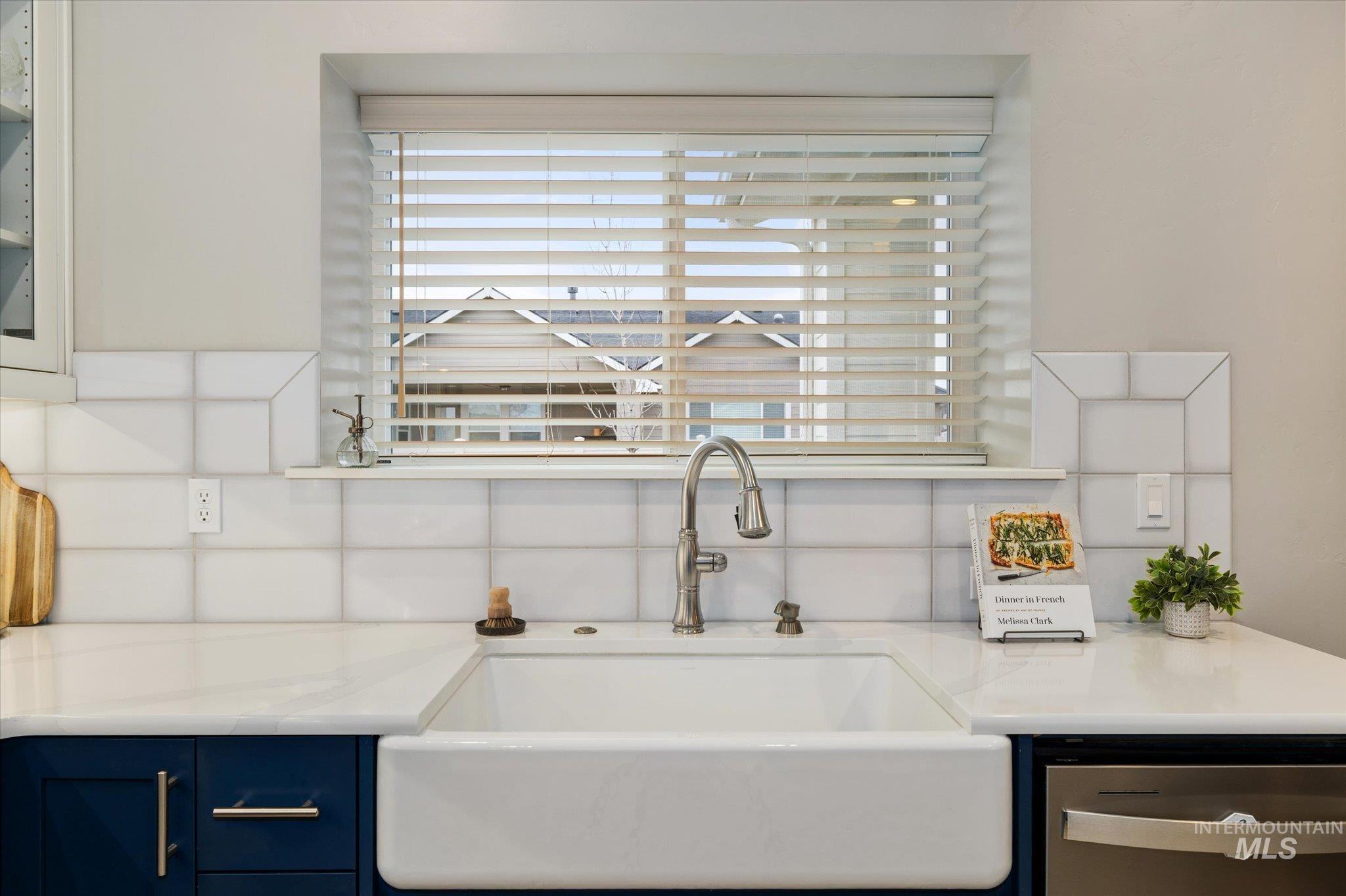 Kitchen view of decorative backsplash, blue cabinets, and stainless steel dishwasher