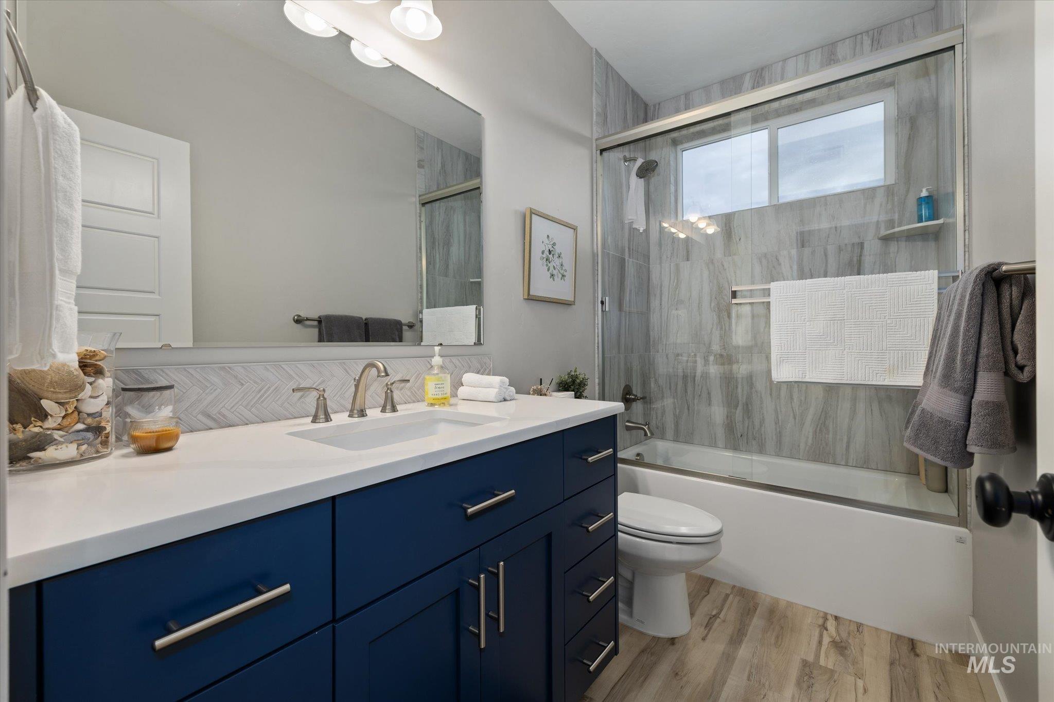 Full bath with vanity, bath / shower combo with glass door, and light wood-style flooring
