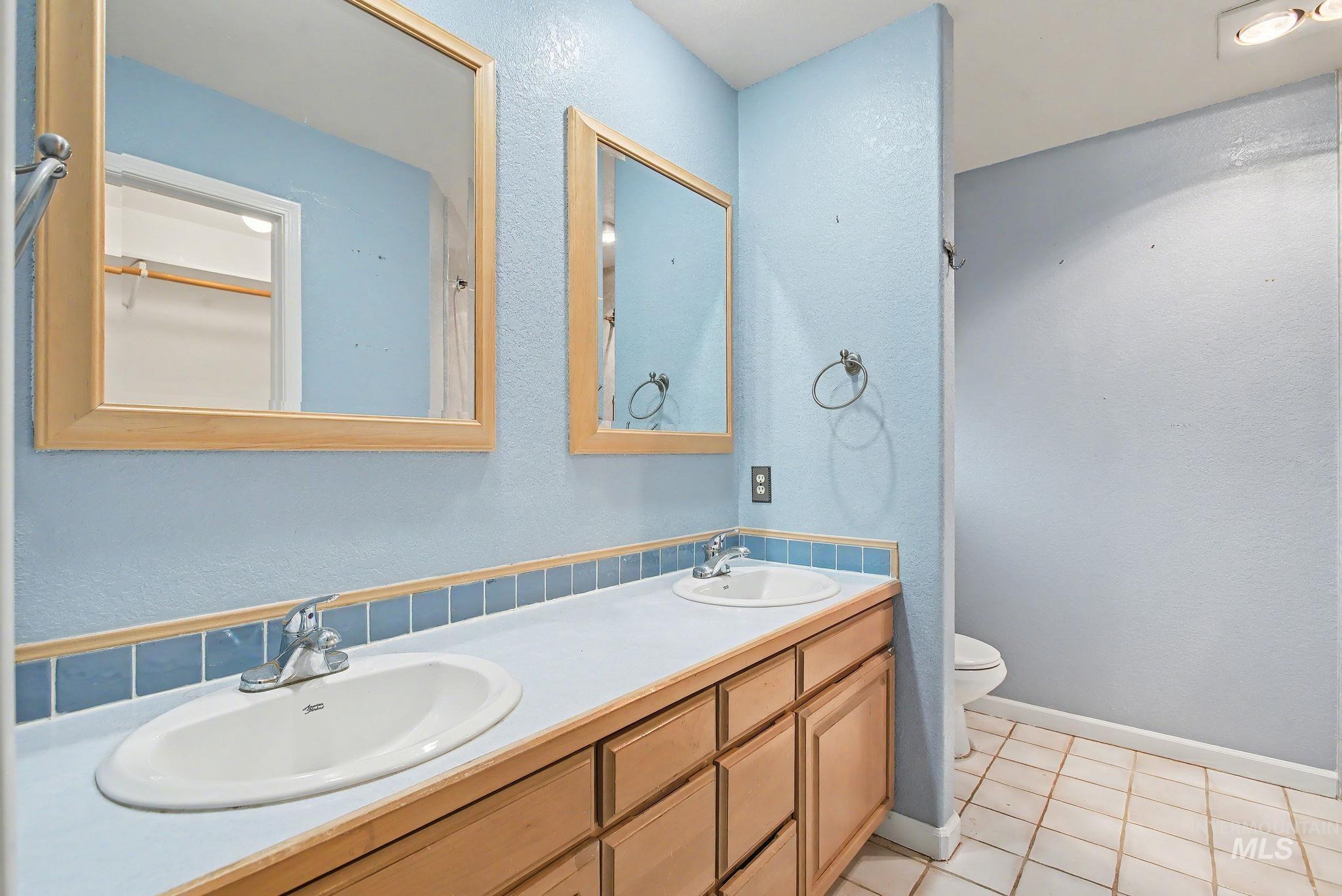 Bathroom with a textured wall, double vanity, and light tile patterned flooring