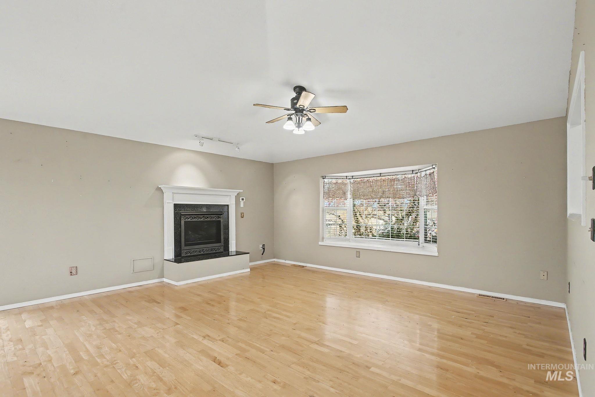 Unfurnished living room featuring a fireplace, rail lighting, light wood finished floors, and a ceiling fan