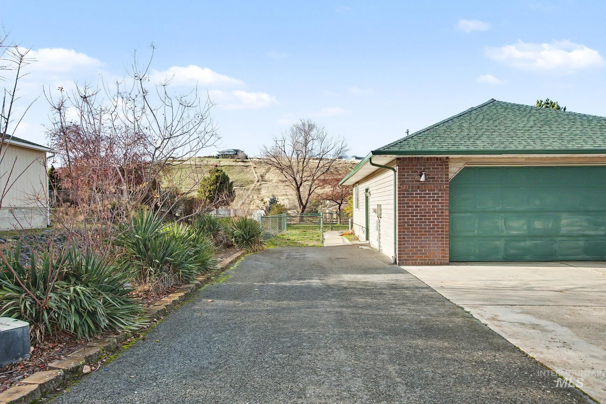 View of side of property with asphalt driveway, brick siding, a shingled roof, a gate, and a garage