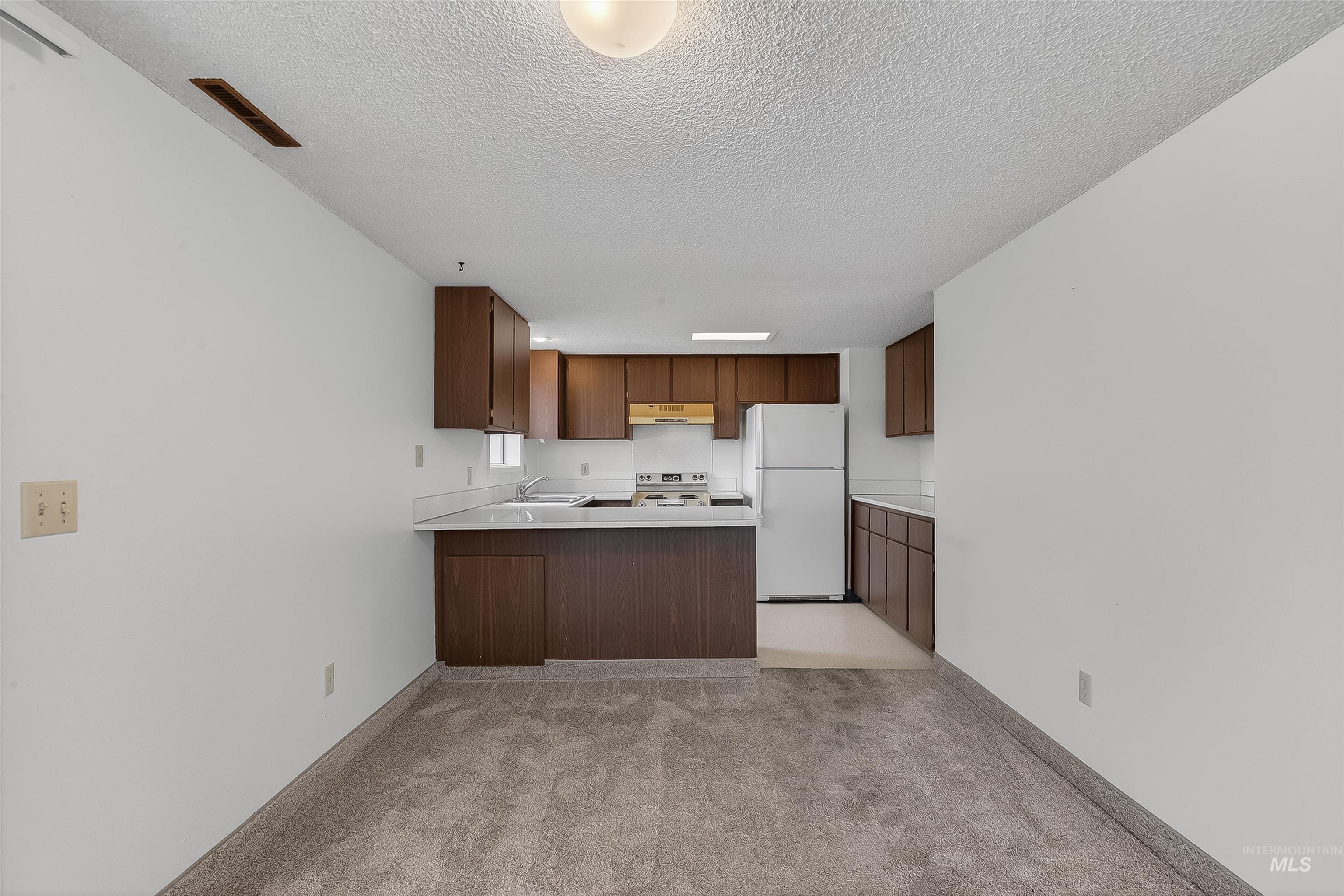 Kitchen with a peninsula, light countertops, freestanding refrigerator, light colored carpet, and a textured ceiling