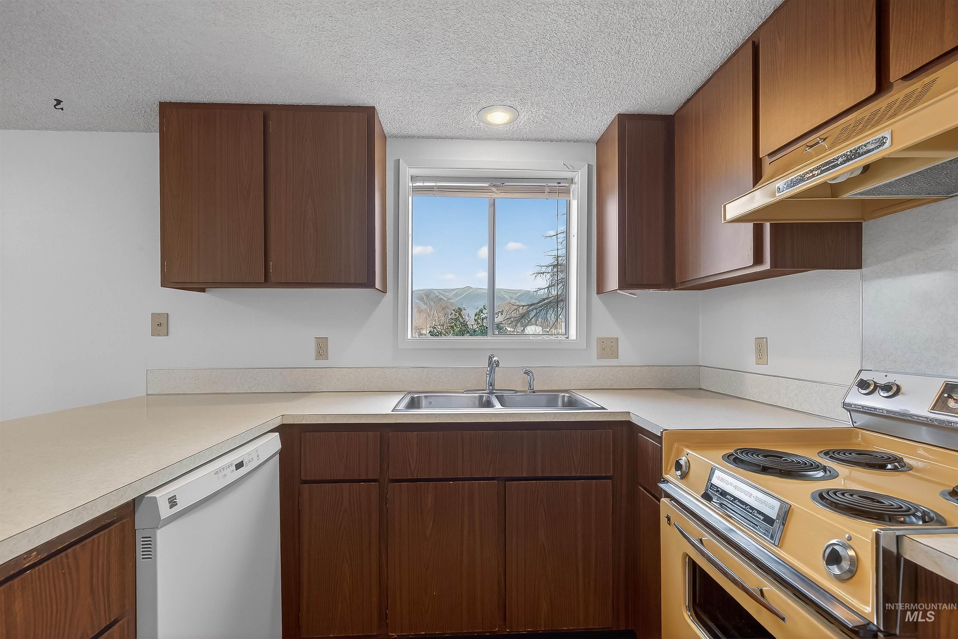 Kitchen featuring range with electric stovetop, dishwasher, under cabinet range hood, light countertops, and a textured ceiling