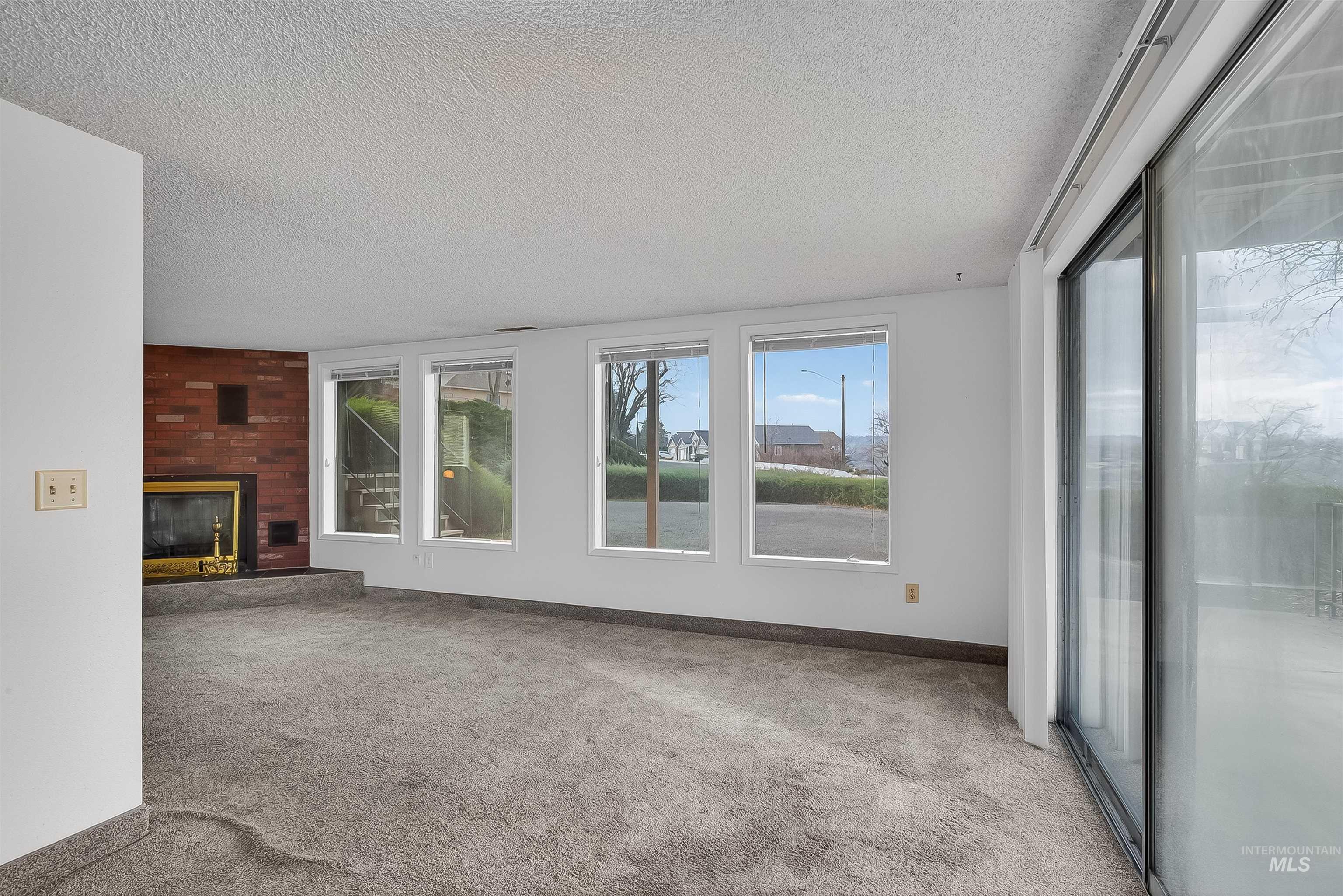 Unfurnished living room featuring a textured ceiling, a fireplace, and light carpet