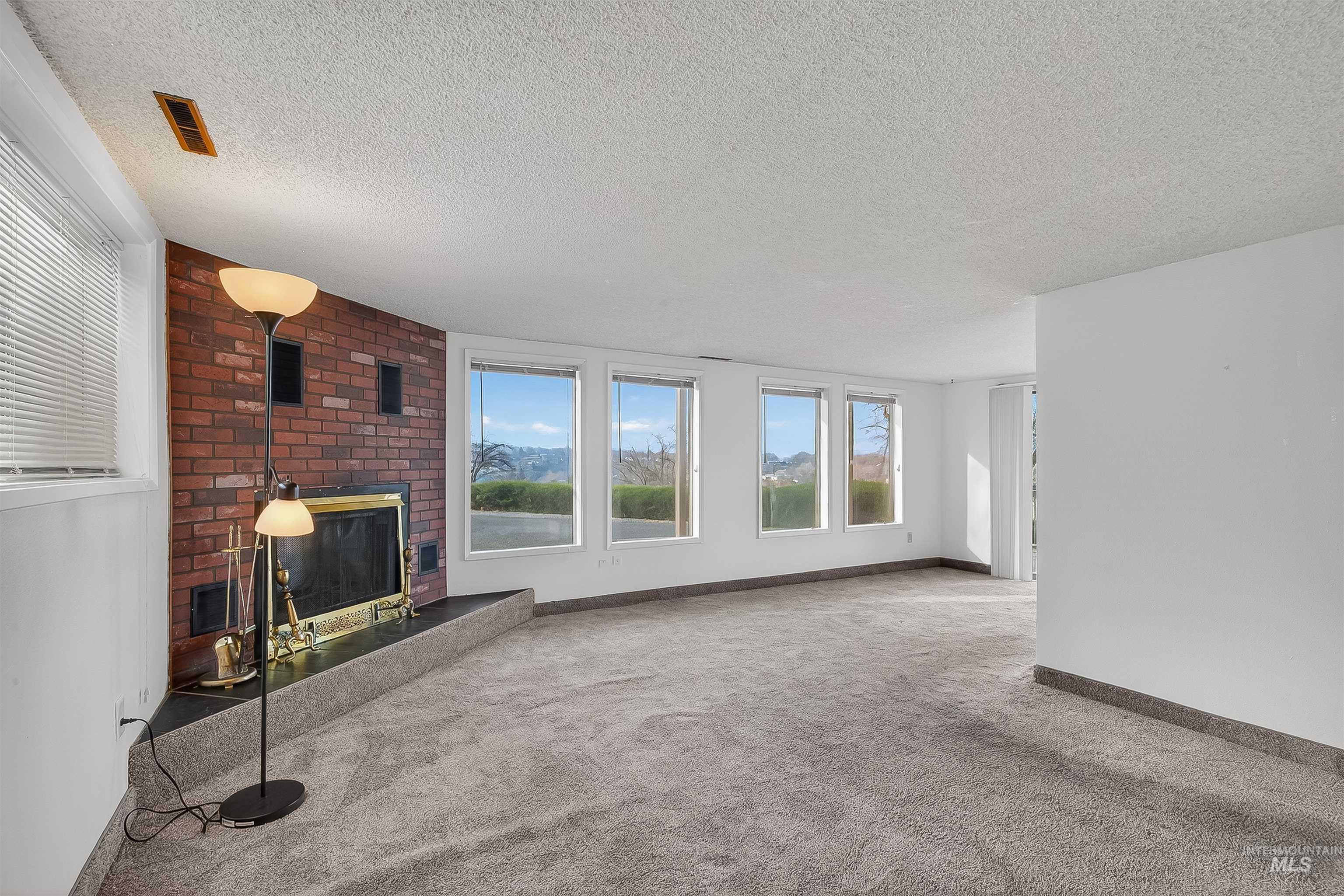 Unfurnished living room featuring carpet flooring, a textured ceiling, and a brick fireplace