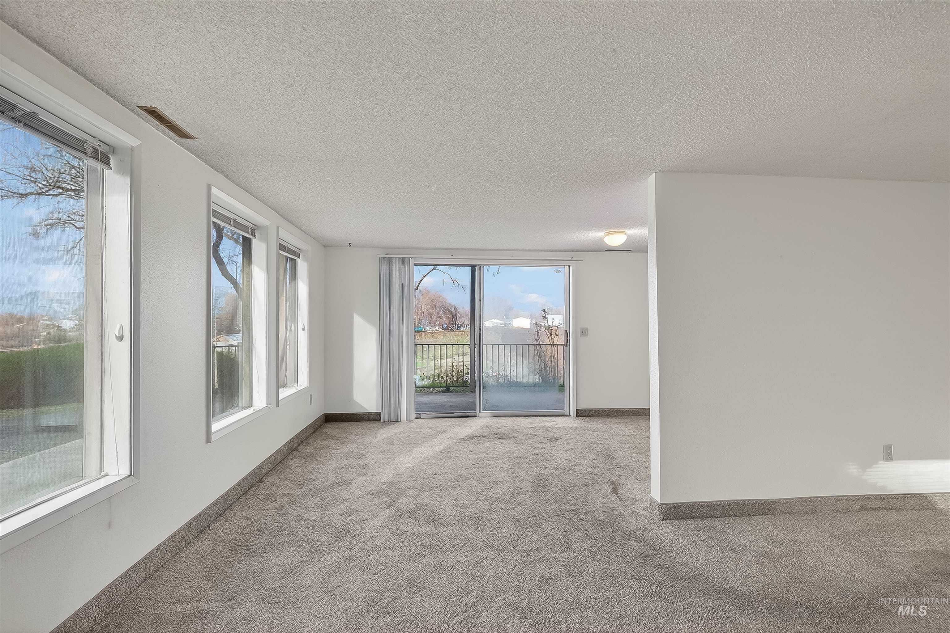 Carpeted spare room featuring a textured ceiling and baseboards