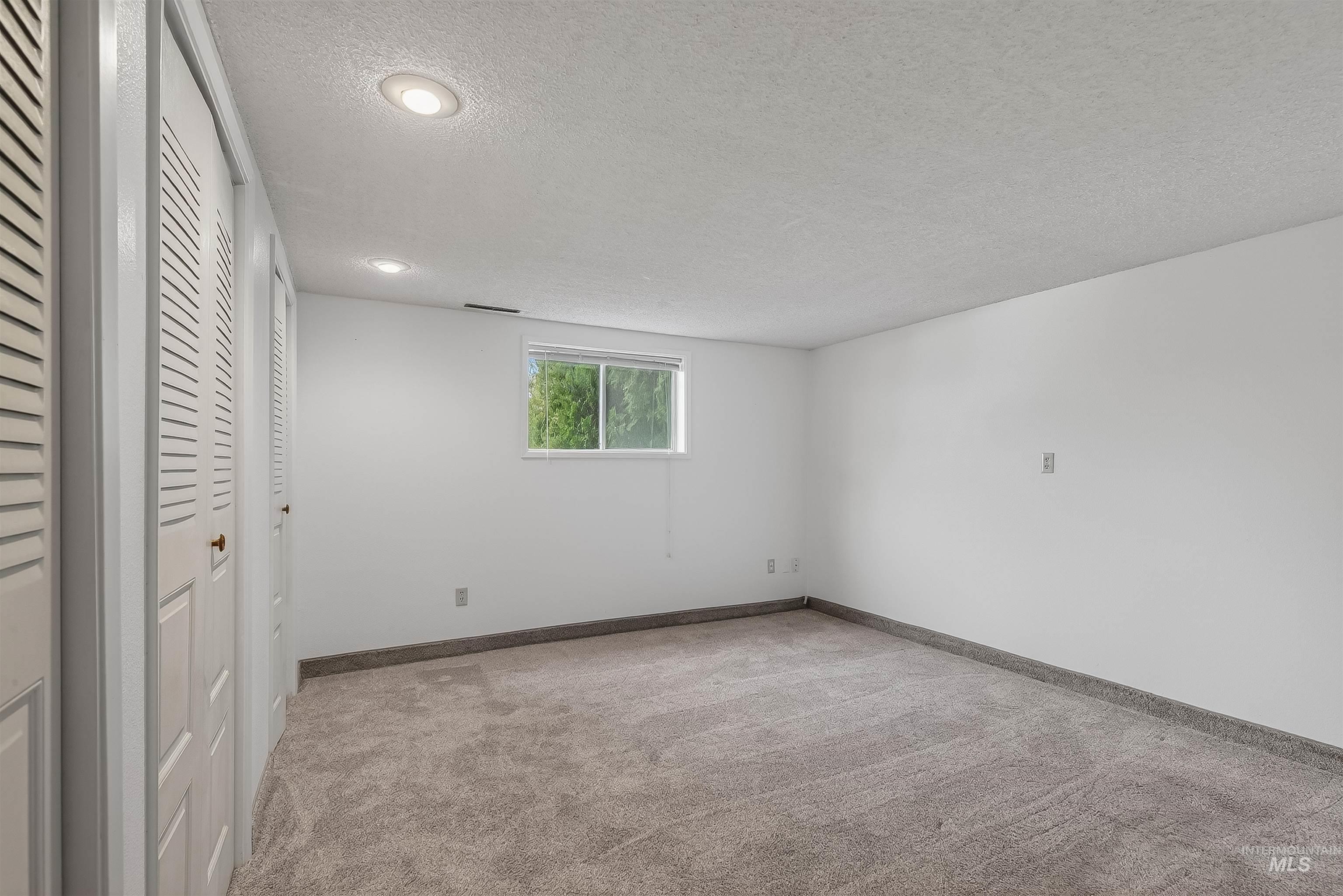 Unfurnished bedroom with two closets, a textured ceiling, and light carpet