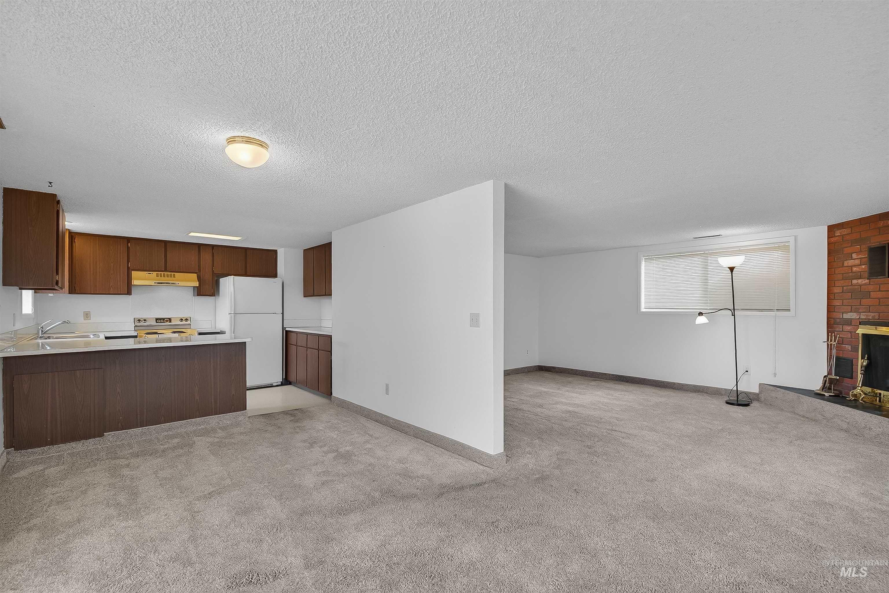Kitchen with open floor plan, a peninsula, light countertops, freestanding refrigerator, and light carpet