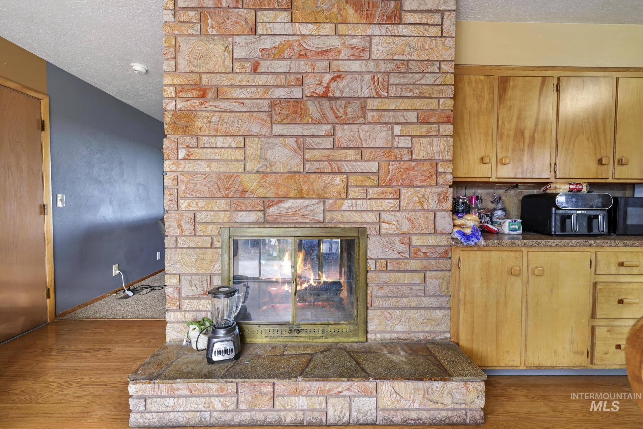 Kitchen with a textured ceiling, light wood-type flooring, a stone fireplace, and black microwave