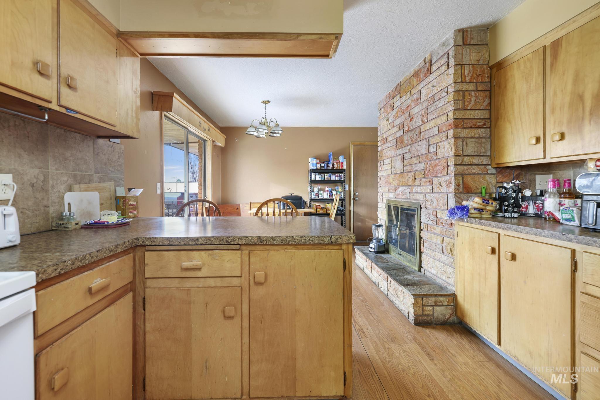 Kitchen with backsplash, a peninsula, a stone fireplace, a chandelier, and light wood-style flooring
