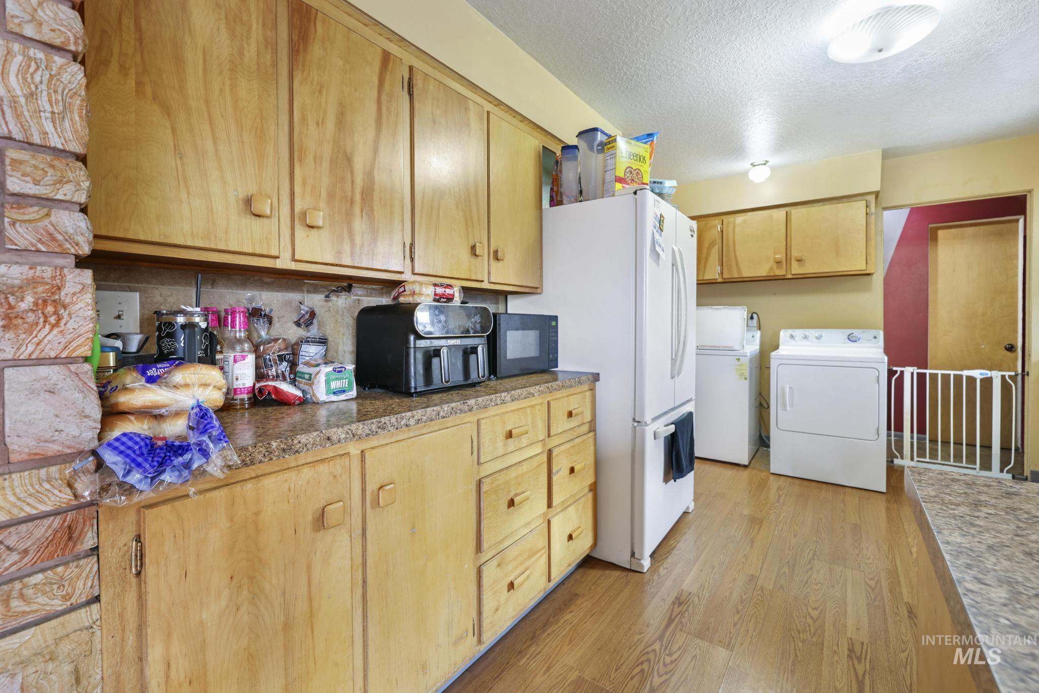 Kitchen featuring a textured ceiling, light wood finished floors, washing machine and dryer, tasteful backsplash, and black microwave