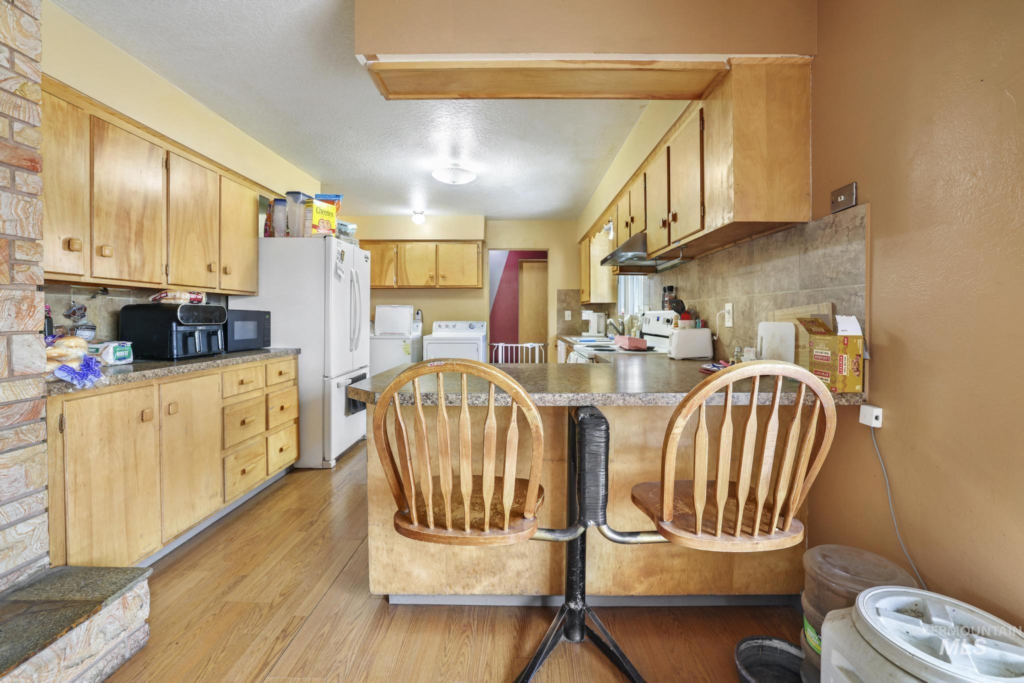 Kitchen with decorative backsplash, light wood finished floors, a breakfast bar, a peninsula, and a textured ceiling