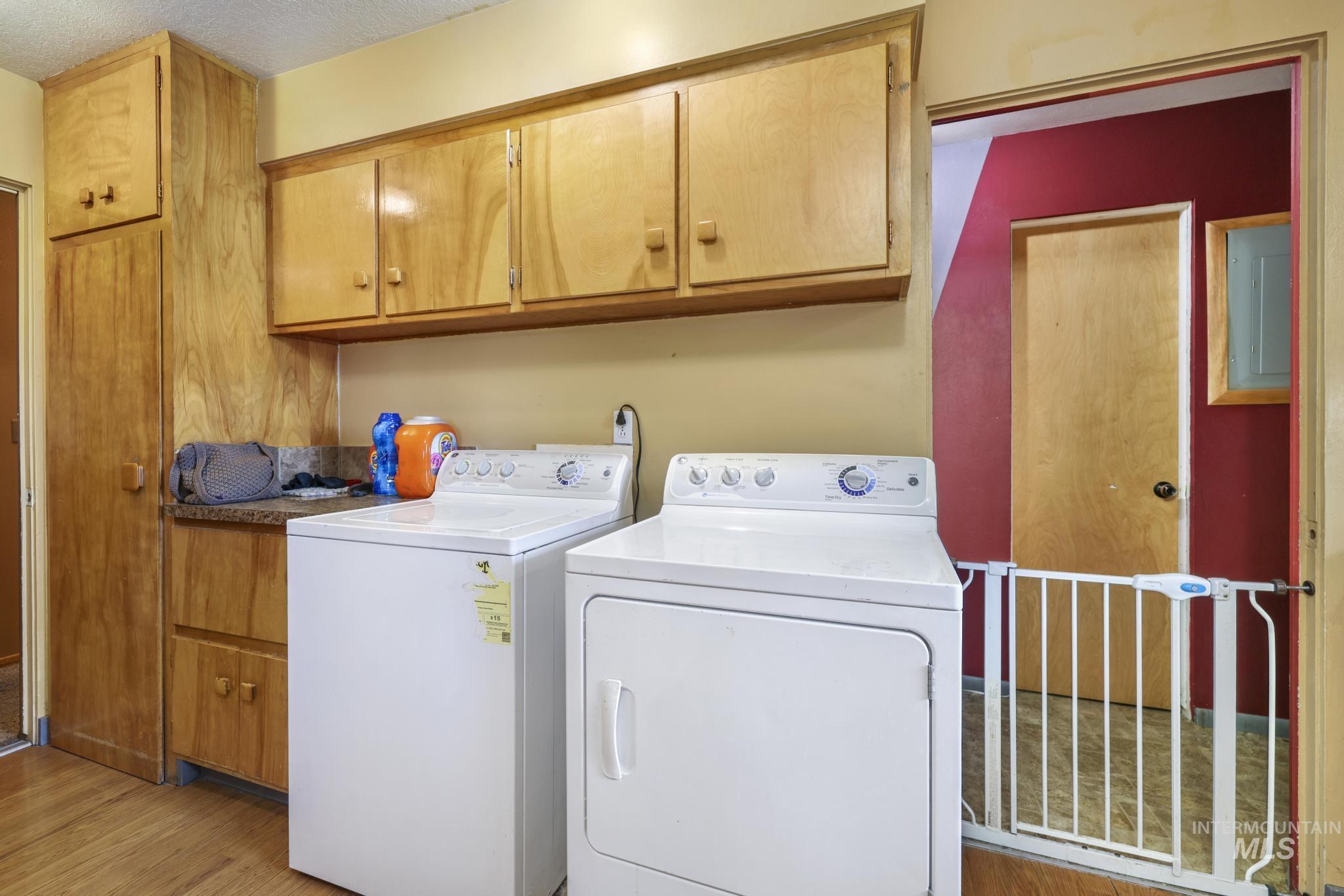 Laundry room featuring washing machine and clothes dryer, cabinet space, light wood-style flooring, a textured ceiling, and electric panel