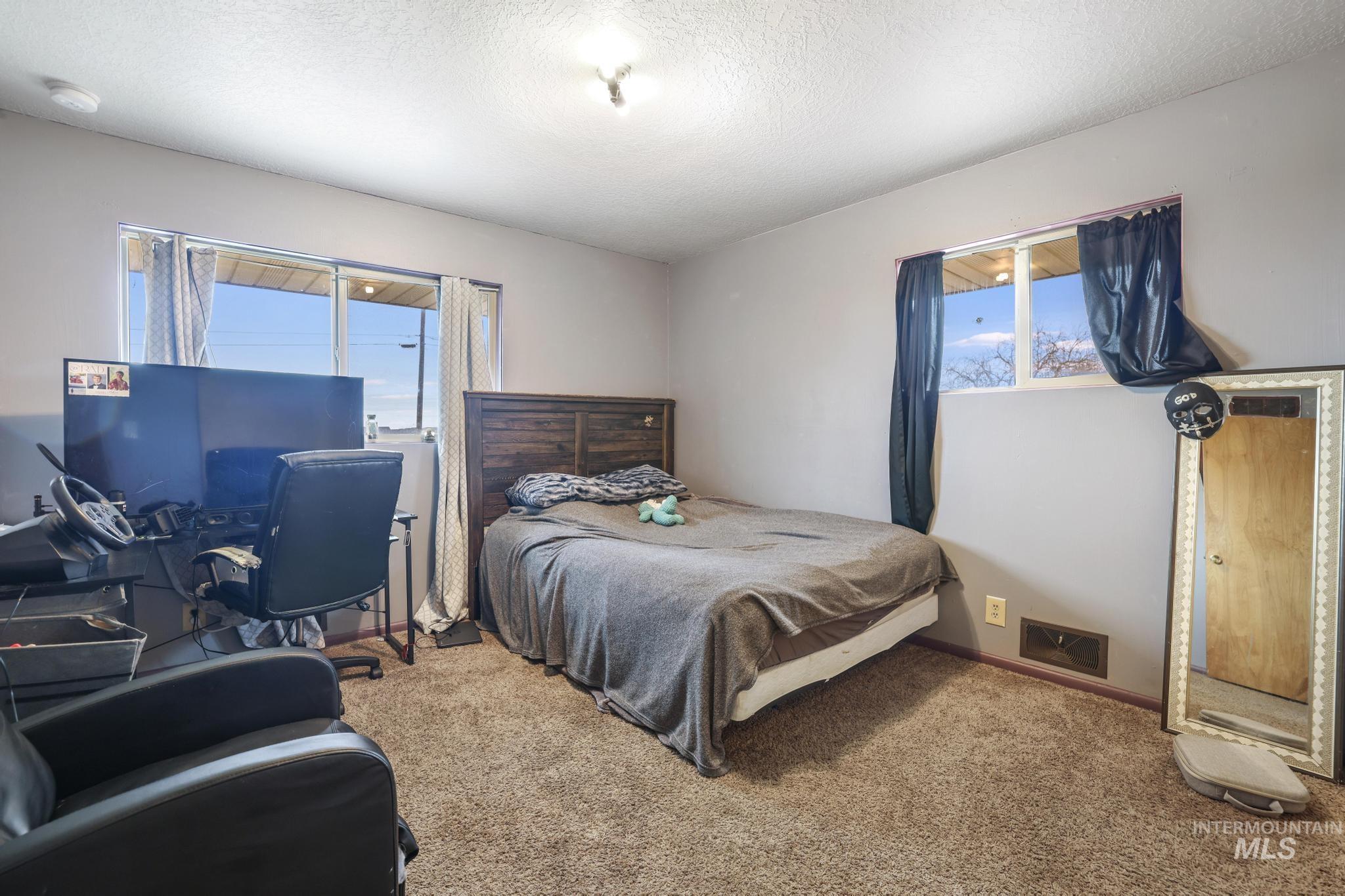 Bedroom with carpet floors, a textured ceiling, and multiple windows