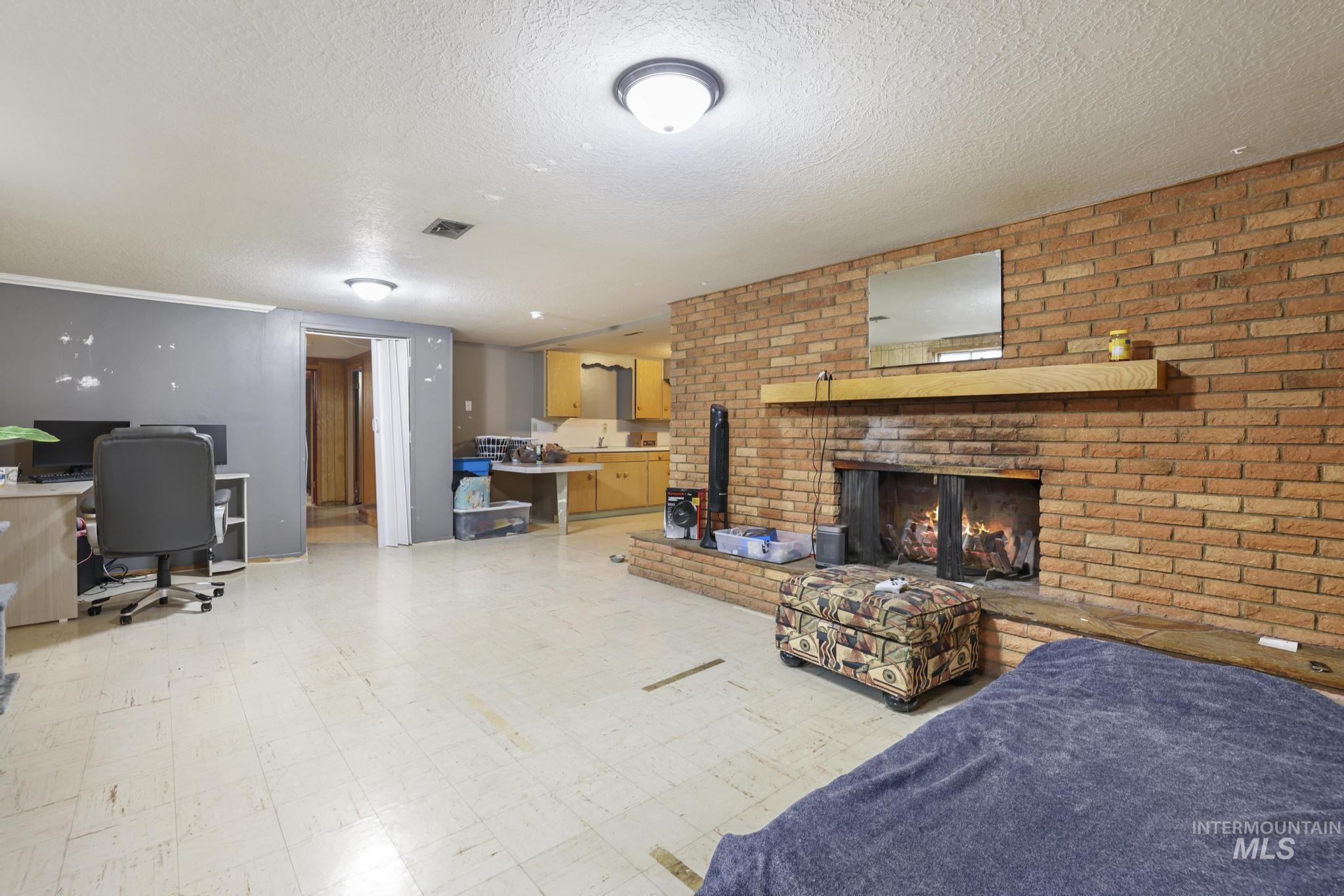 Living area with tile patterned floors, an office area, a fireplace, a textured ceiling, and brick wall