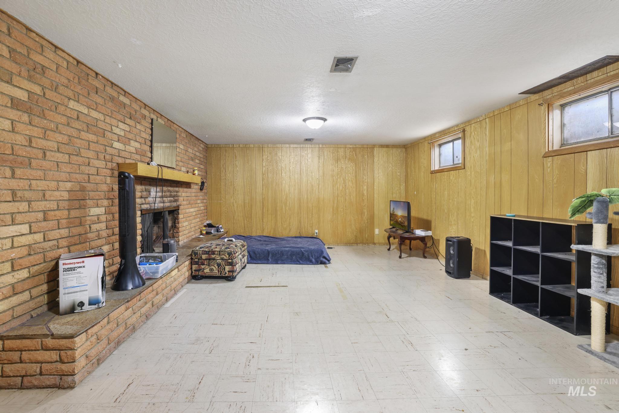 Bedroom featuring tile patterned floors, wooden walls, a brick fireplace, and a textured ceiling