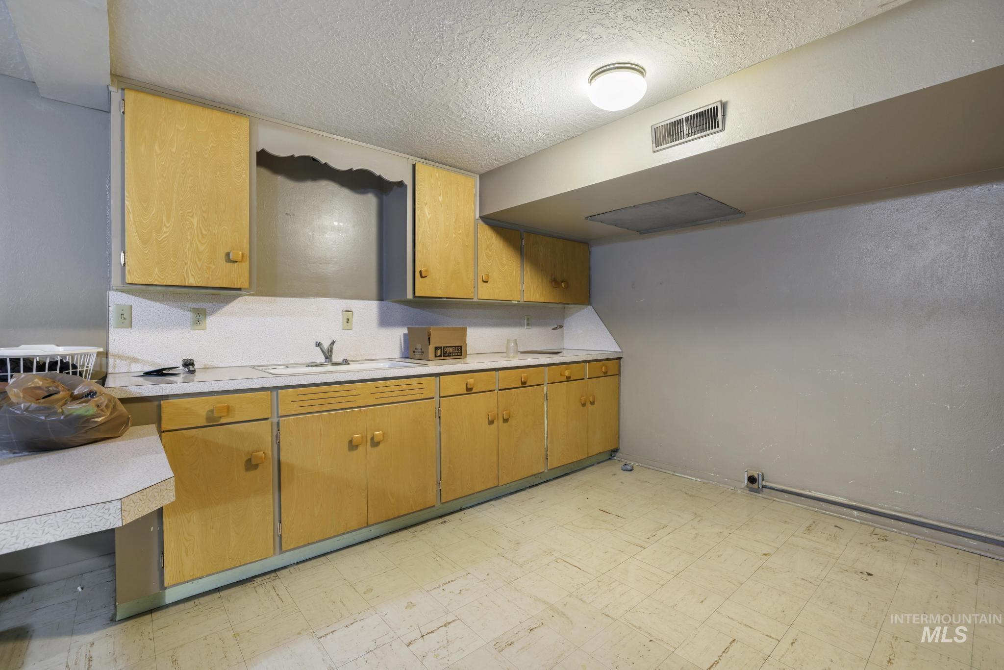 Kitchen featuring light floors, light countertops, a textured ceiling, and brown cabinetry