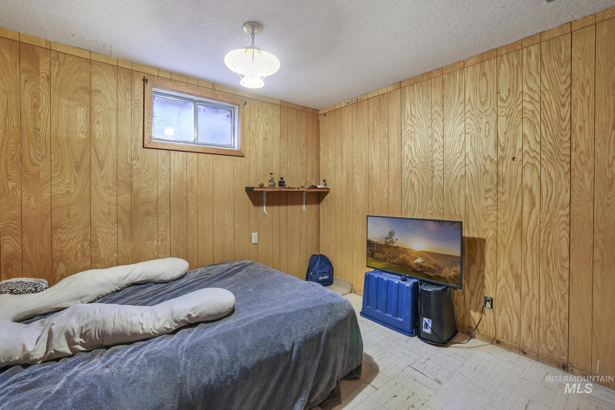Bedroom with wooden walls, a textured ceiling, and light flooring