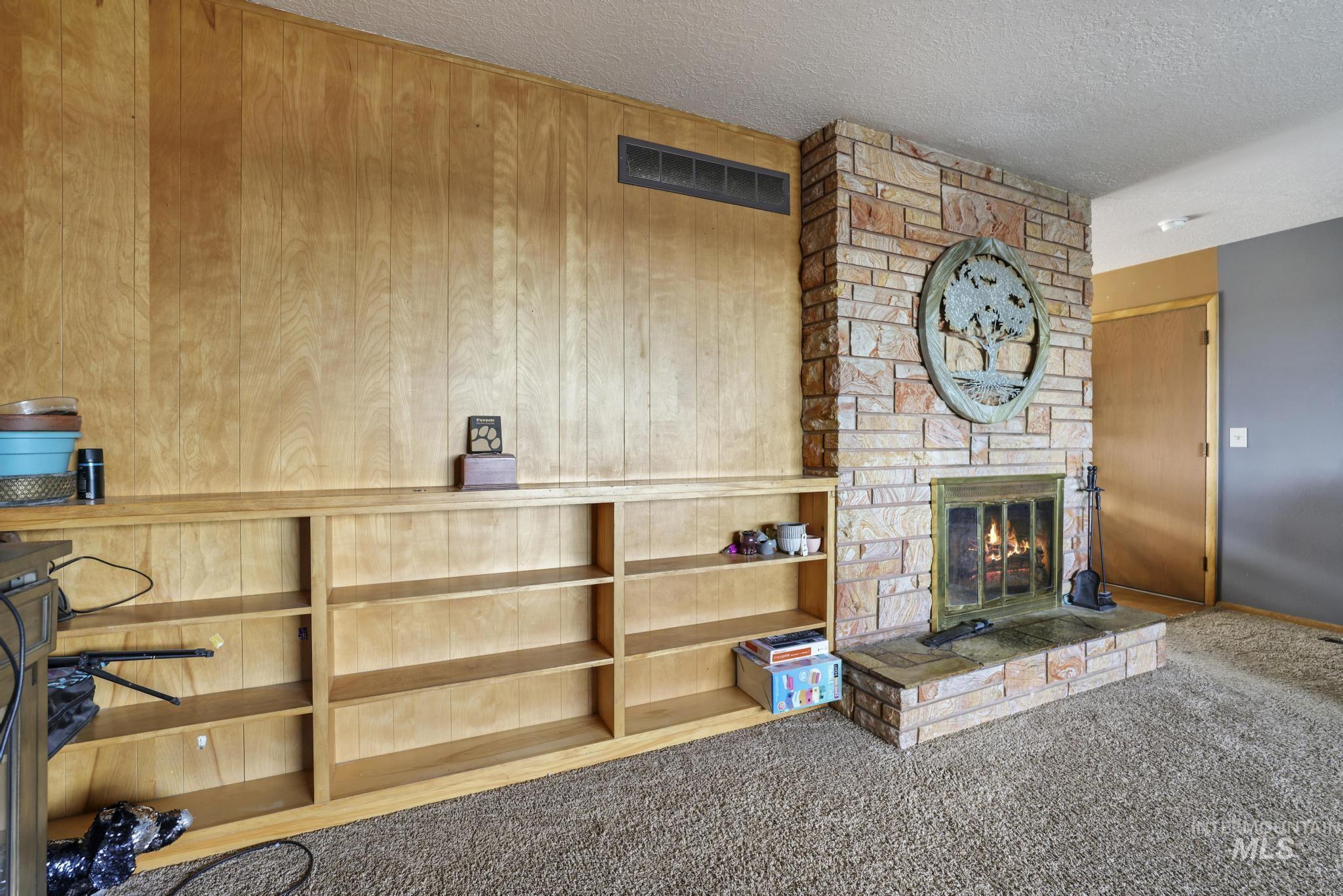 Unfurnished living room featuring carpet, a stone fireplace, a textured ceiling, and wood walls