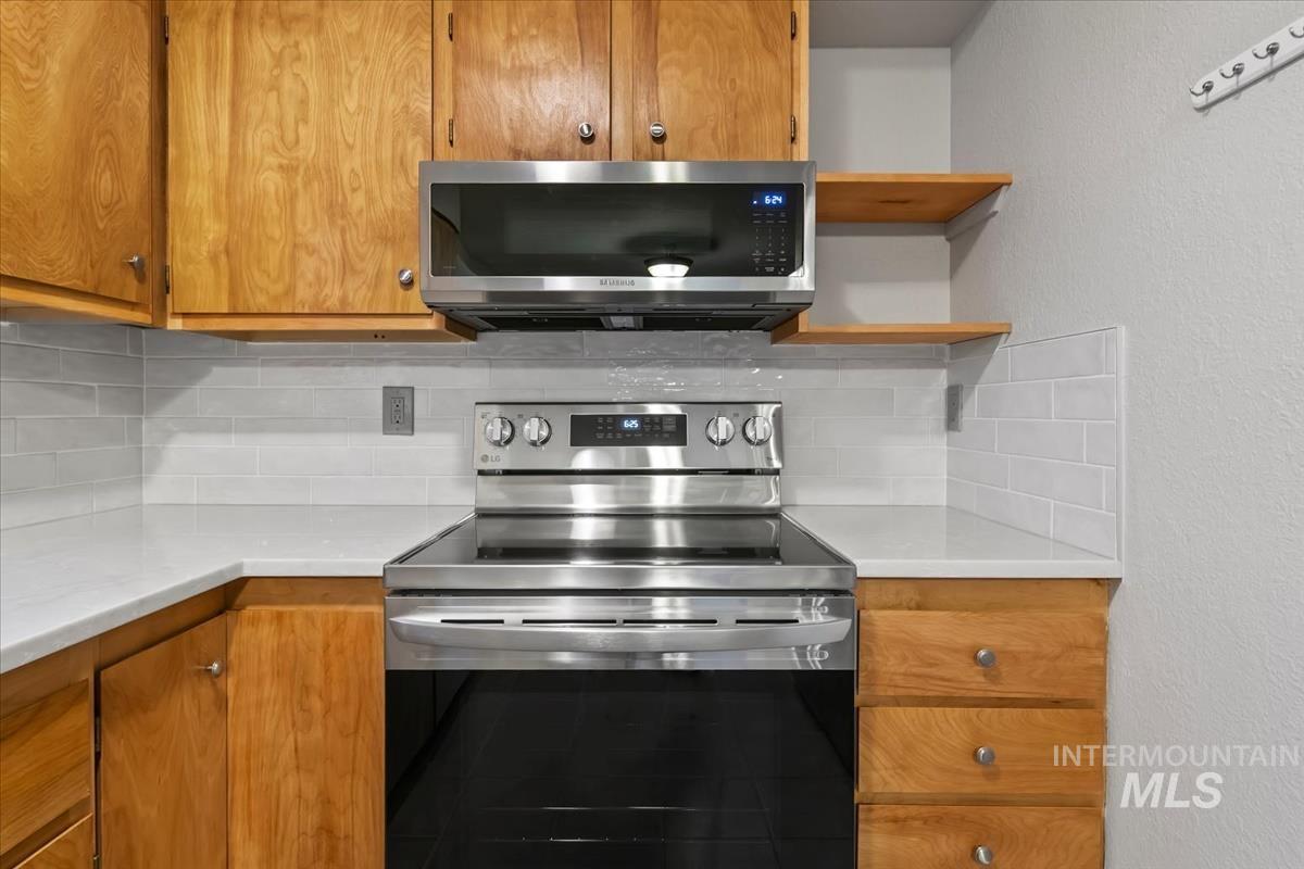 Kitchen featuring appliances with stainless steel finishes, a textured wall, open shelves, brown cabinets, and tasteful backsplash