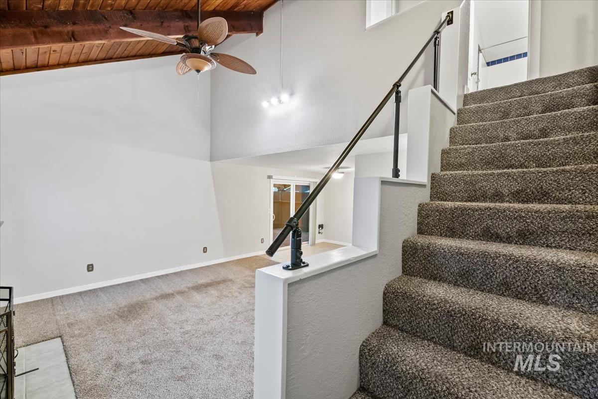 Staircase featuring carpet flooring, a wood ceiling with exposed beams, ceiling fan, and a towering ceiling