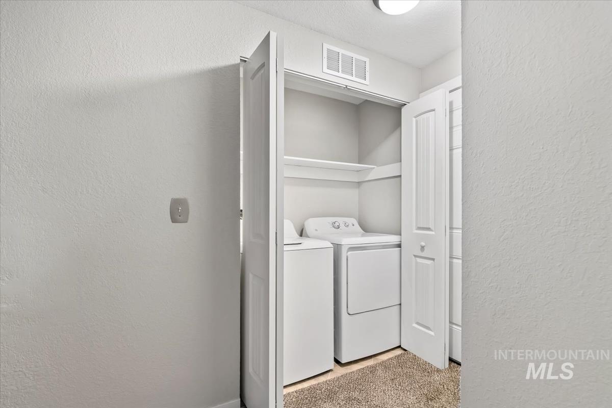 Laundry room featuring a textured wall, independent washer and dryer, and light carpet