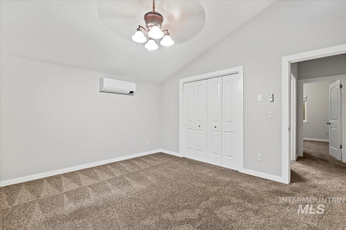 Unfurnished bedroom with vaulted ceiling, carpet, a closet, ceiling fan, and a wall mounted air conditioner