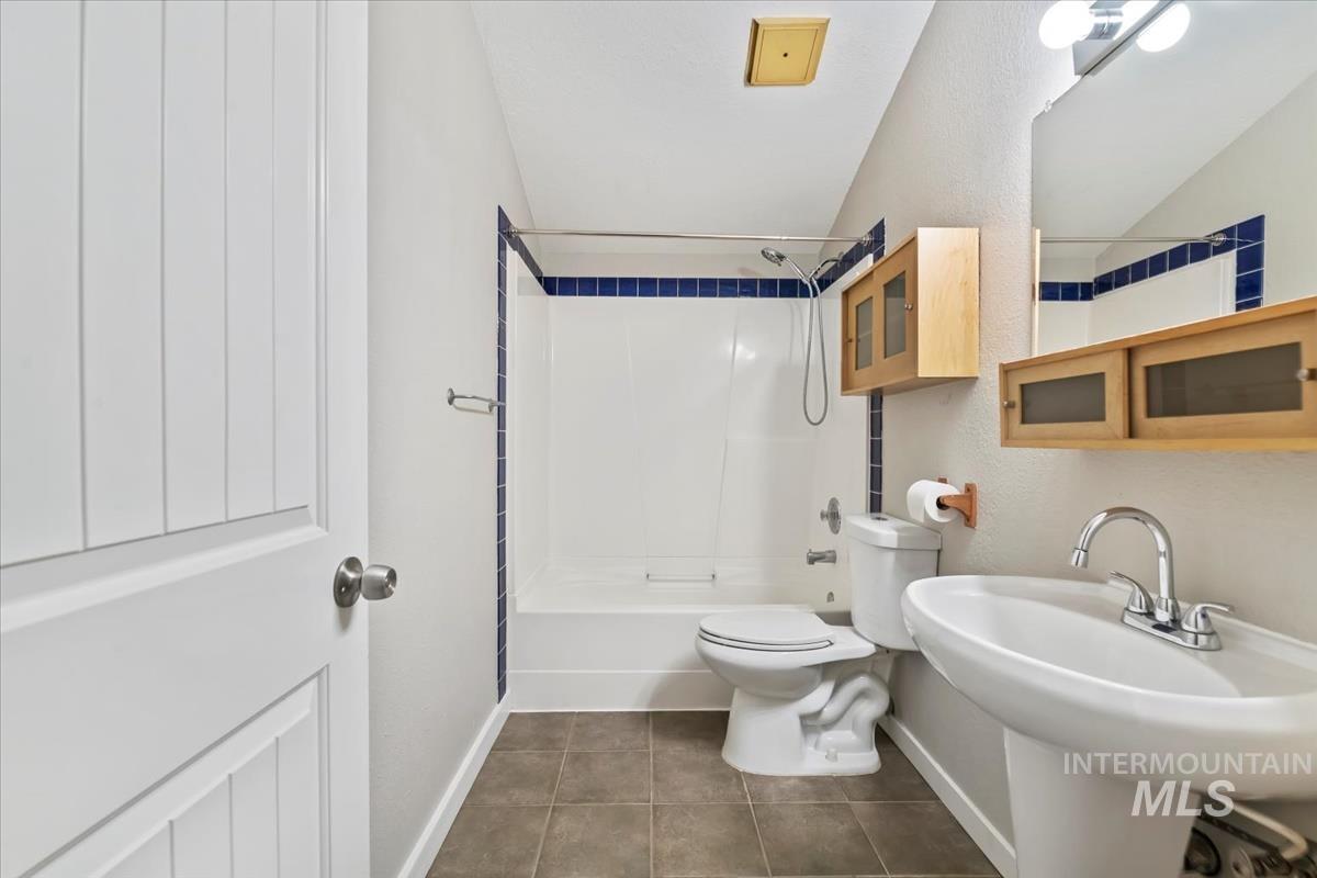 Bathroom featuring shower / bathtub combination, dark tile patterned floors, vaulted ceiling, and a textured wall