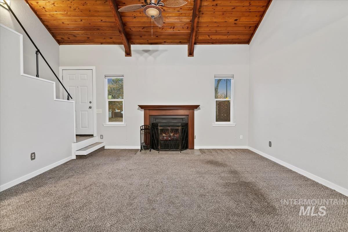 Unfurnished living room featuring wood ceiling, carpet, a fireplace with flush hearth, a ceiling fan, and stairway