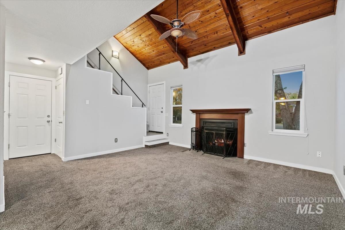 Unfurnished living room with wood ceiling, carpet, a fireplace with flush hearth, ceiling fan, and stairway