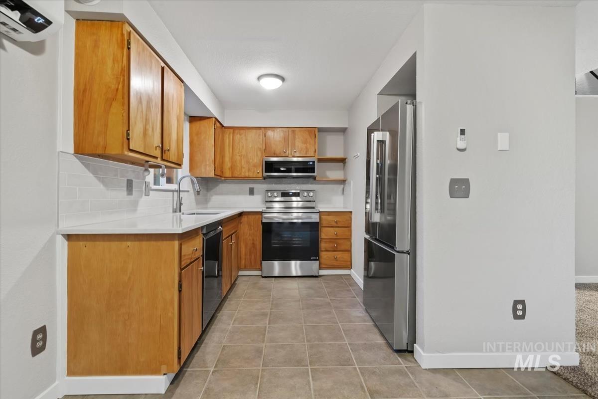 Kitchen featuring brown cabinetry, open shelves, appliances with stainless steel finishes, light tile patterned floors, and light stone countertops