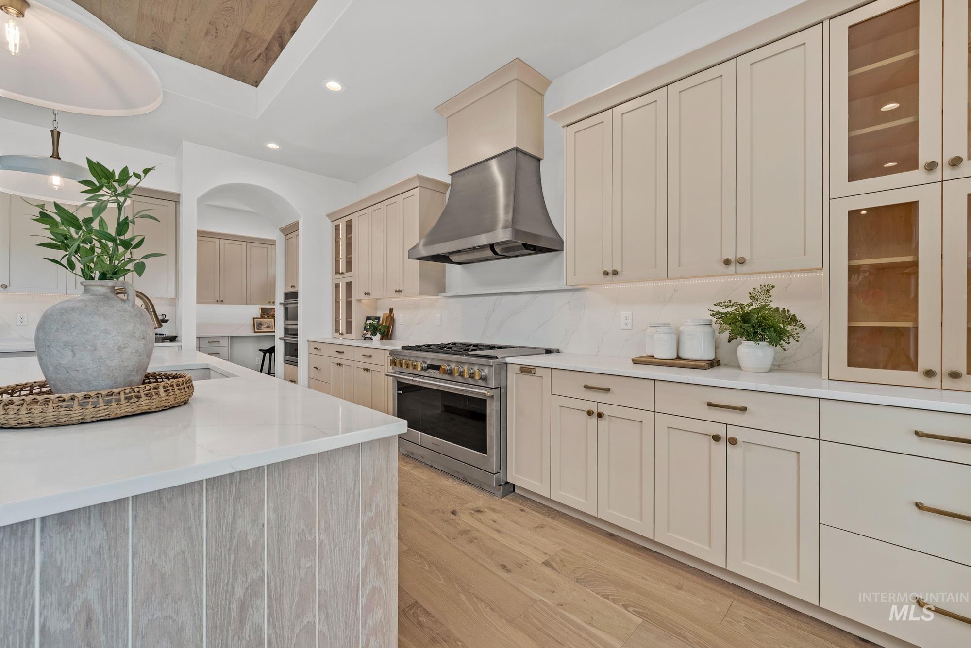 Kitchen with high end stainless steel range oven, recessed lighting, light wood-style flooring, light stone counters, and glass insert cabinets