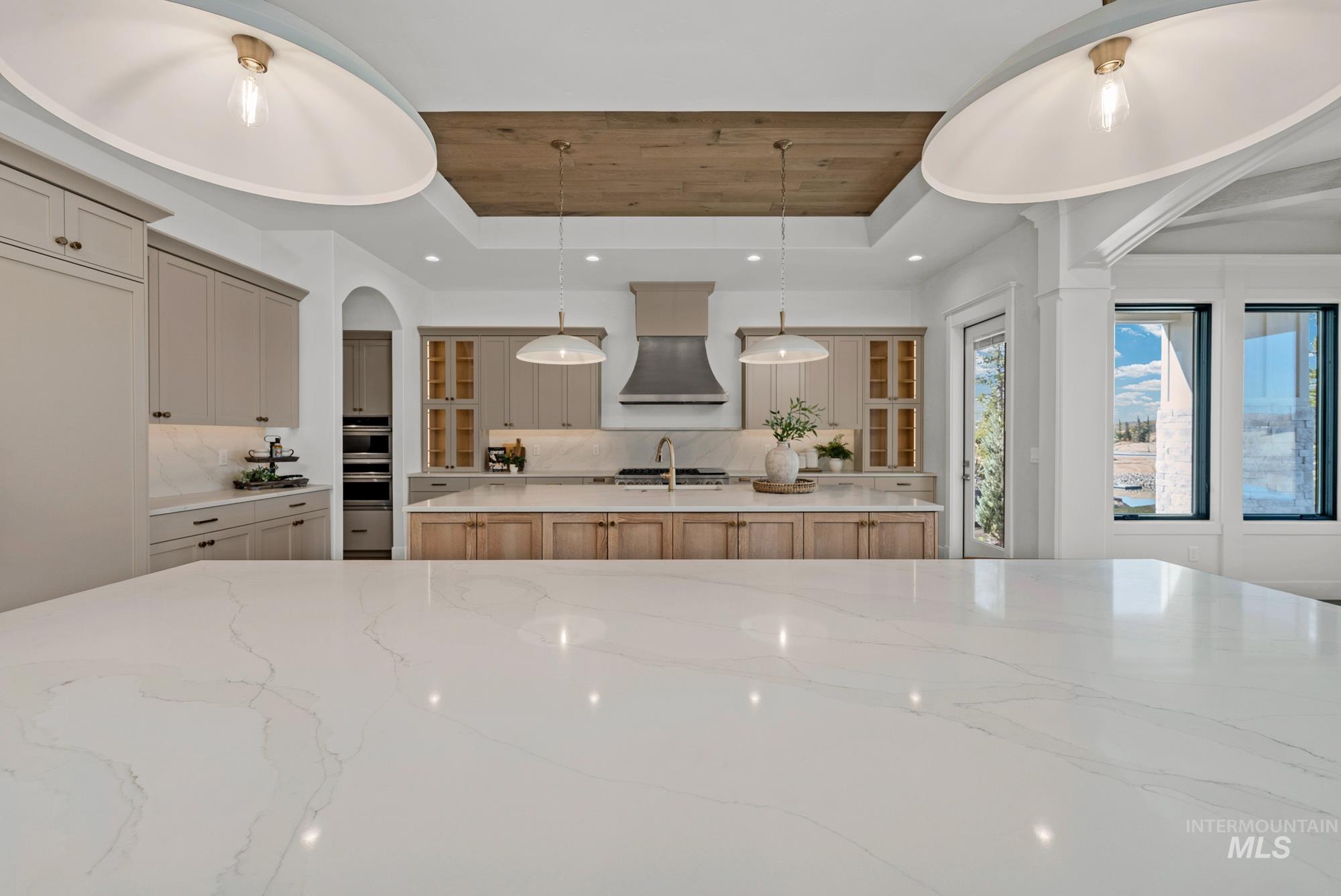 Kitchen with arched walkways, light stone counters, pendant lighting, wooden ceiling, and a raised ceiling