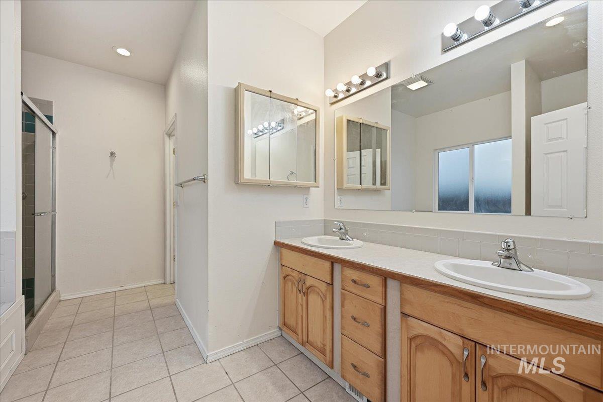 Bathroom with double vanity, light tile patterned floors, and a stall shower